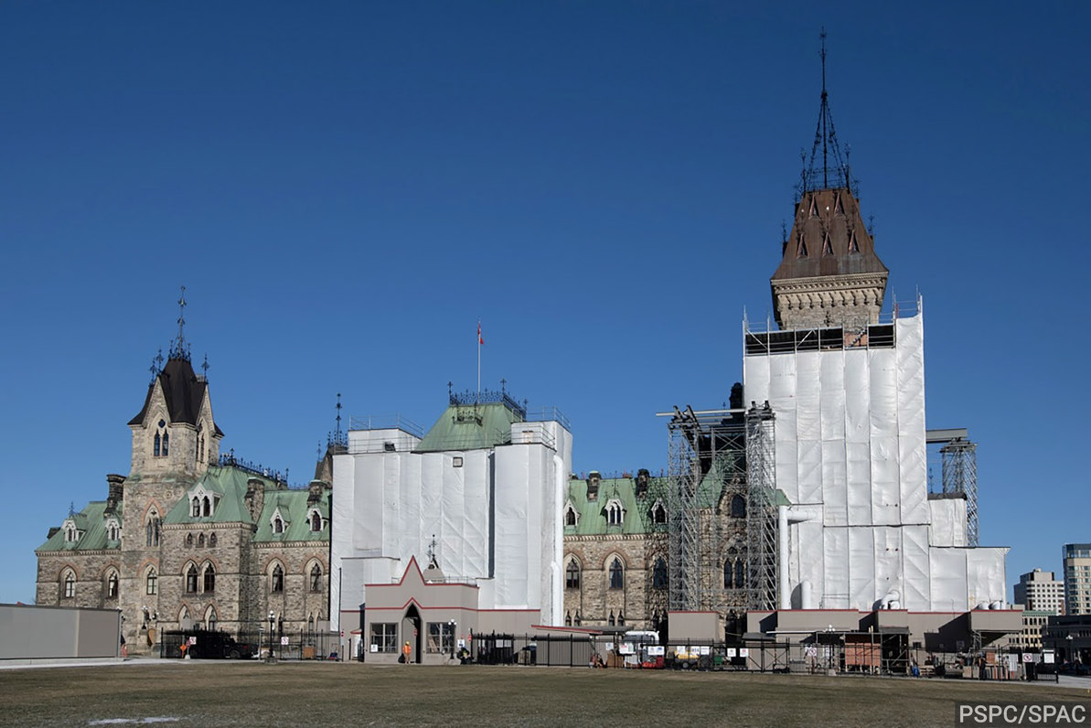 Édifice de l’Est de la Colline du Parlement, partiellement entouré d’échafaudages et de bâches blanches.