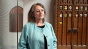 Senator Frances Lankin stands inside the Senate of Canada Building with the old doors of the Senate Chamber in Centre Block in the background.