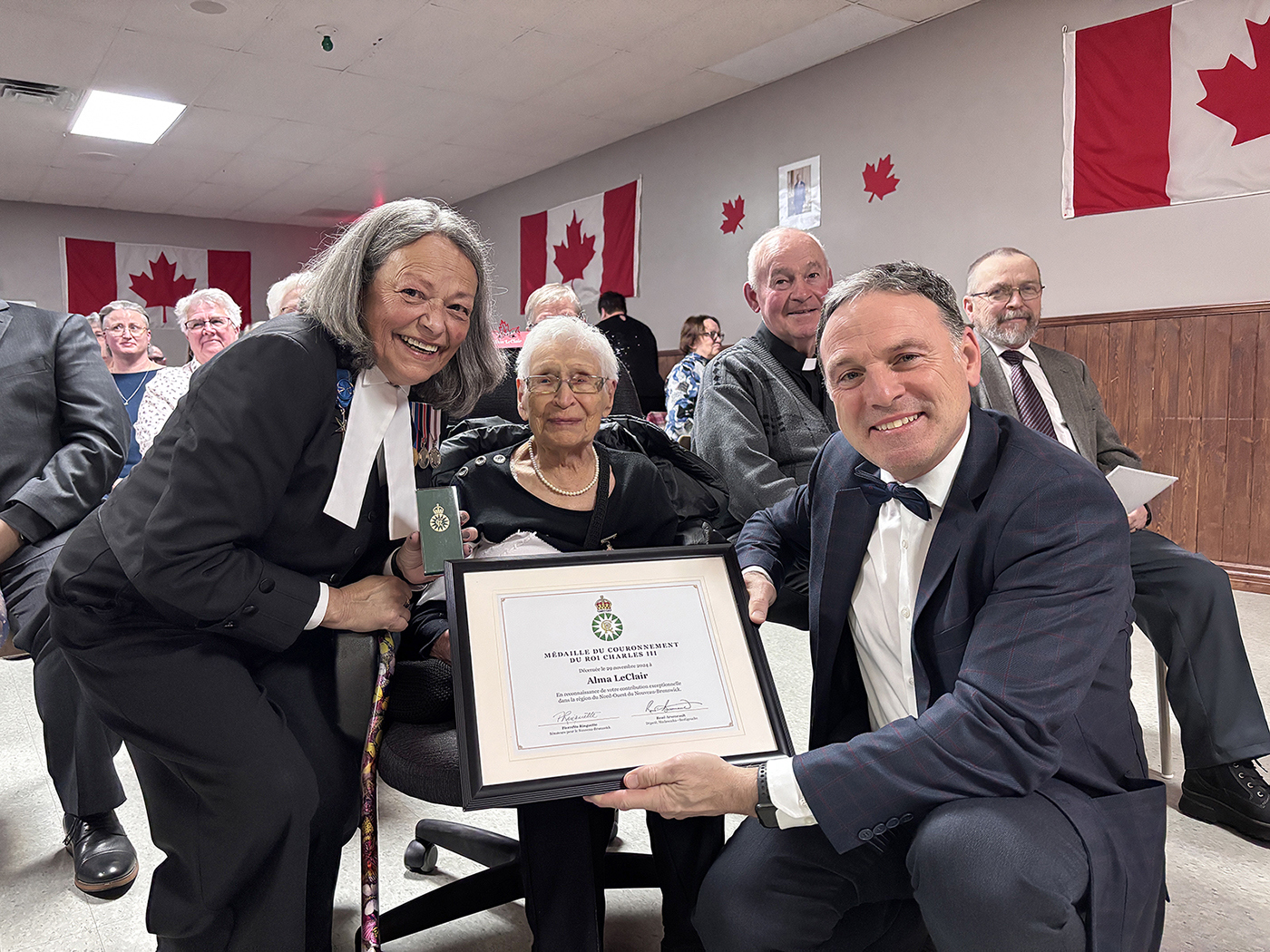 La sénateure Ringuette remet une médaille du couronnement du roi Charles III à Alma LeClair avec René Arseneault, alors député de Madawaska-Restigouche, à Sainte-Anne-de-Madawaska, au Nouveau-Brunswick, le 29 novembre 2024. (Photo fournie par : Bureau de la sénateure Pierrette Ringuette)