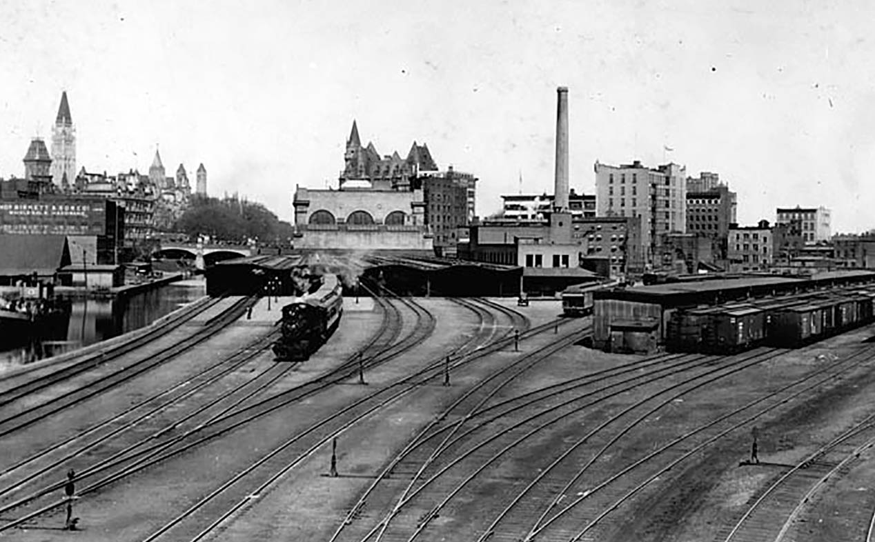 Passenger rail lines used to run into downtown Ottawa along the Rideau Canal. Passengers disembarked at Union Station, now the Senate of Canada Building, under the steel-and-glass train sheds in the centre of the photo. An adjacent freight railyard occupied what is now the Rideau Centre shopping mall.
