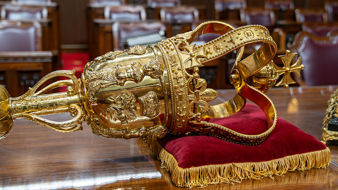 A close-up of the Senate Mace resting on a red cushion with gold fringe on a table in the Senate Chamber.