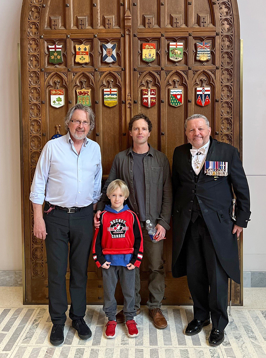 Le sénateur Kutcher pose pour une photo aux côtés de son fils Matt, de son petit-fils Sebastian et de l’huissier du bâton noir, J. Greg Peters, devant les portes d’origine de l’antichambre du Sénat, dans l’édifice du Sénat du Canada. (Crédit photo : Bureau du sénateur Stan Kutcher)
