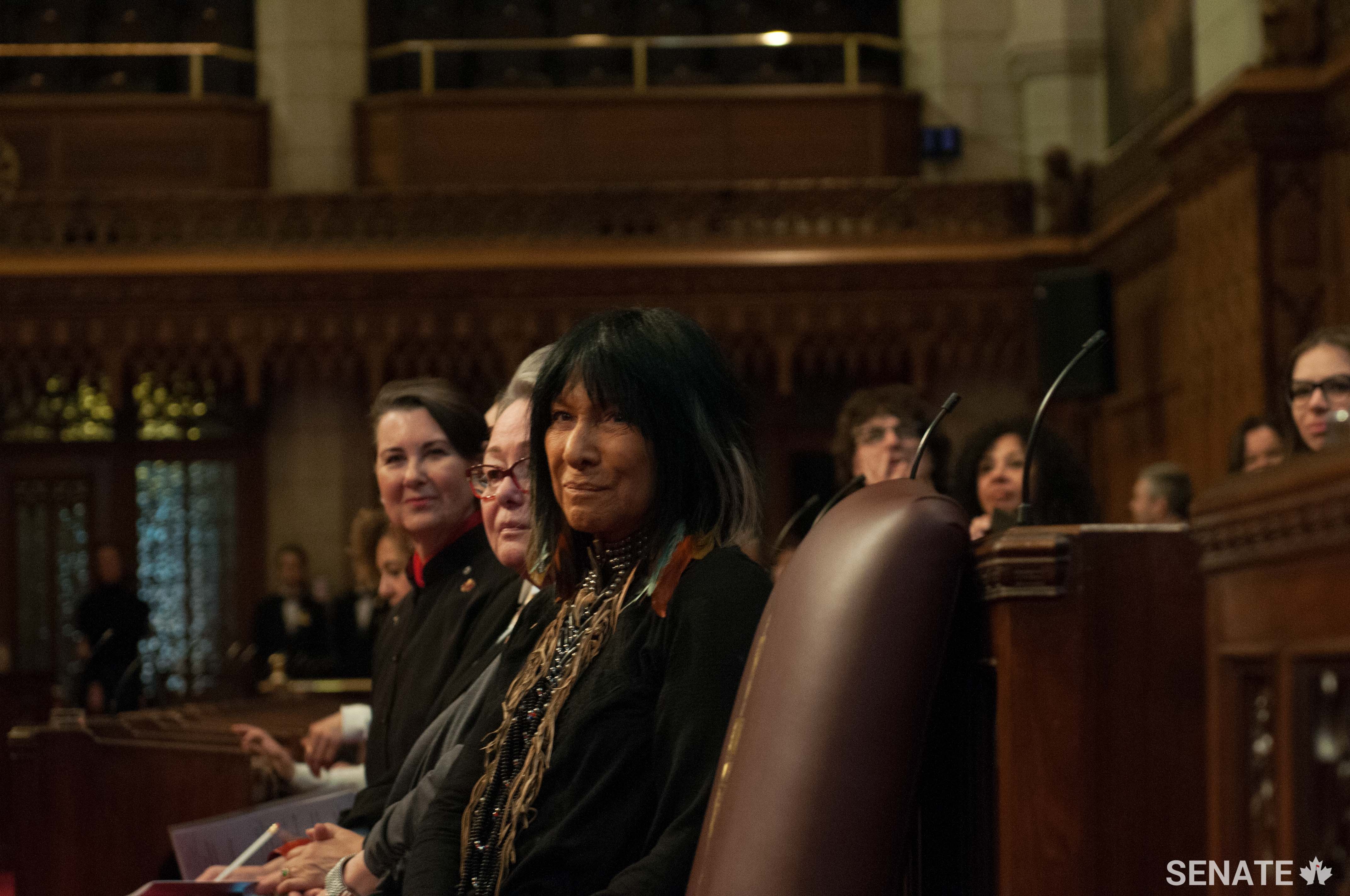 Left to right: Senator McPhedran, Senator Lovelace Nicholas and Buffy Sainte-Marie watch and listen as guest musicians perform in the Senate Chamber.