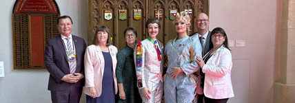 A group of senators and drag performers pose for a photo in the Senate of Canada Building.  