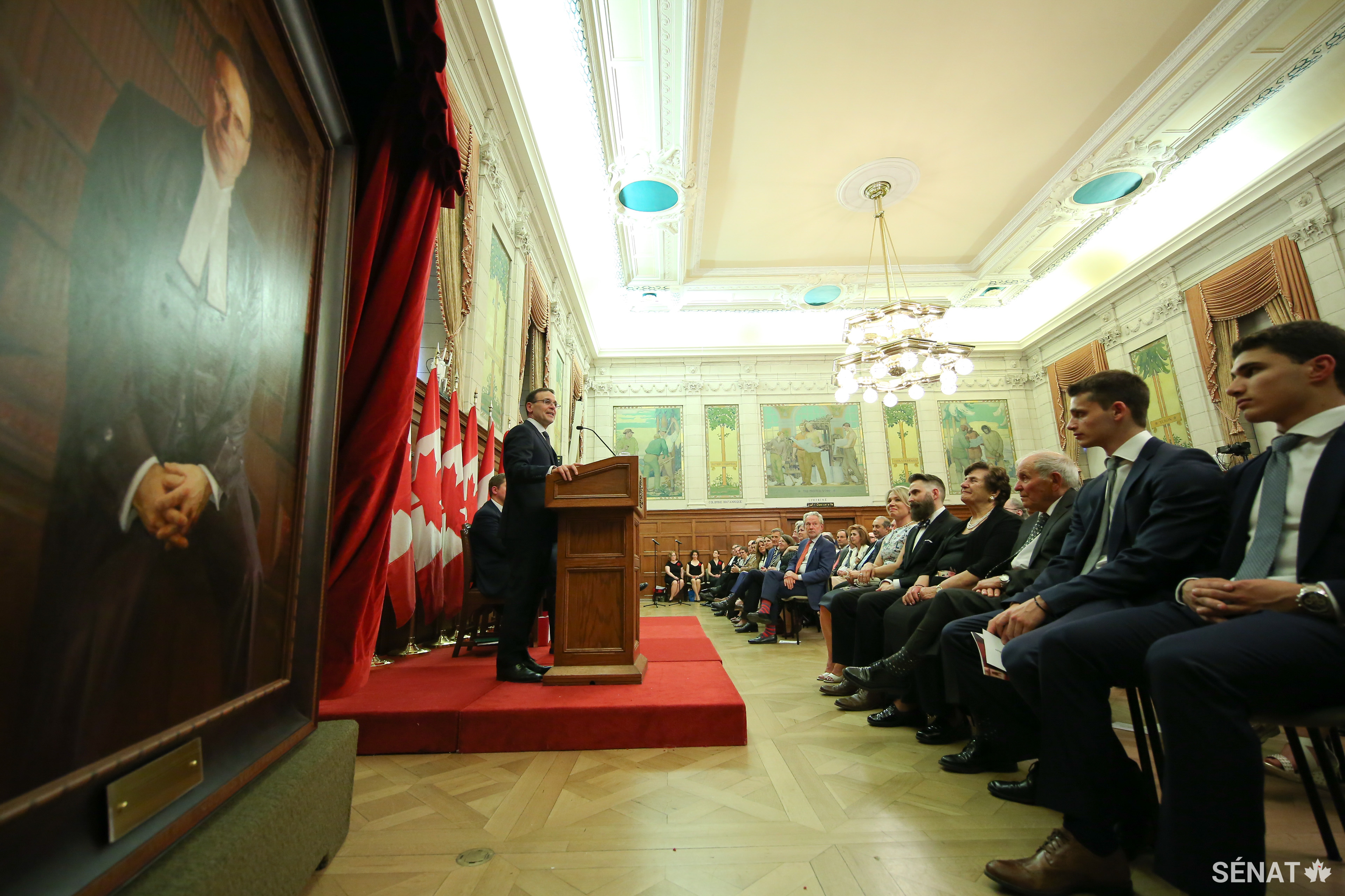 Les invités écoutent un discours dans une salle comble de l’édifice du Centre dans le cadre d’une cérémonie organisée pour le dévoilement du portrait du sénateur Leo Housakos, le 44e Président du Sénat.