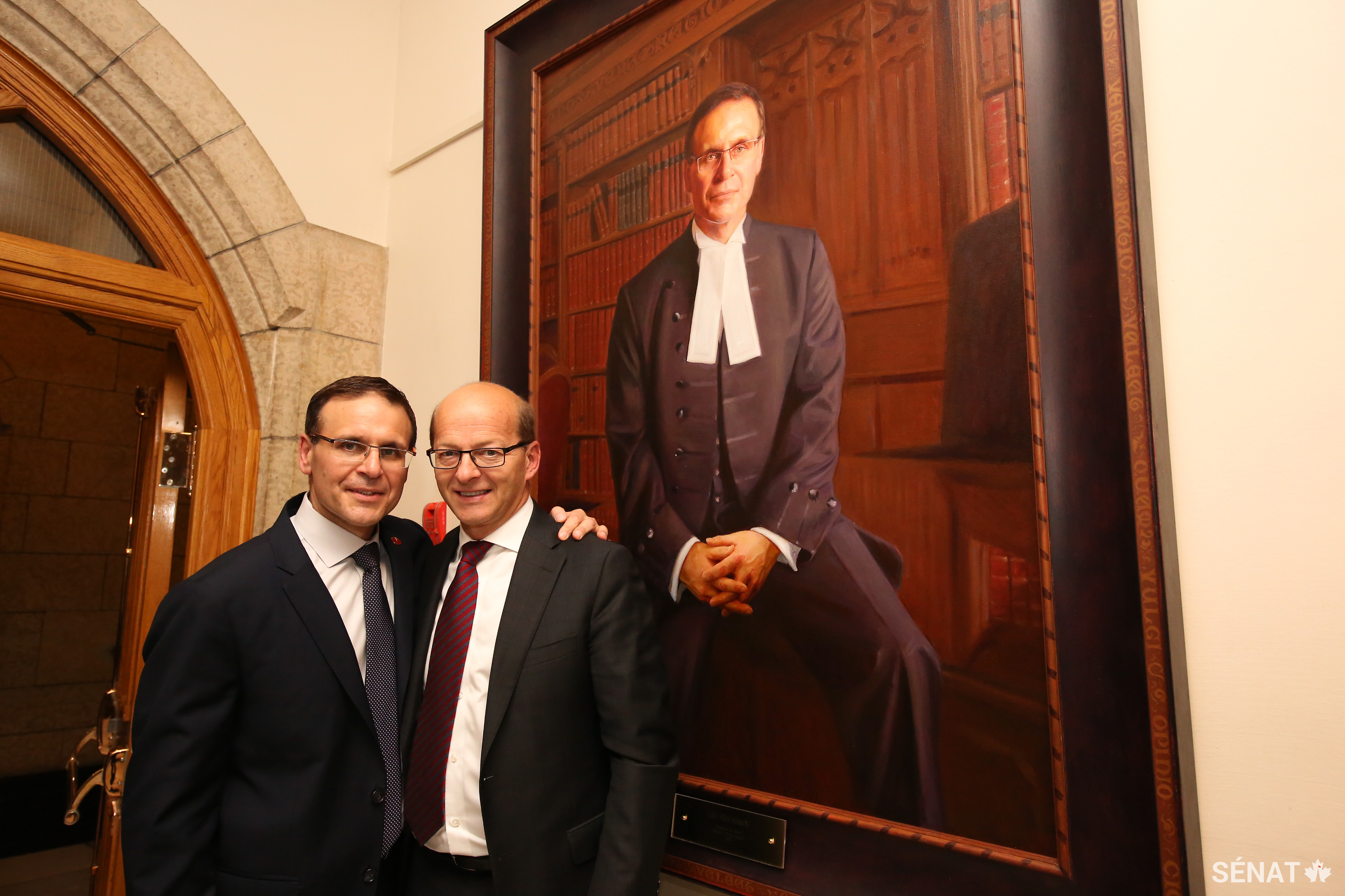 Le sénateur Housakos, à gauche, partage un moment avec son ami et collègue, le sénateur Claude Carignan, peu de temps après que le portrait commémorant le mandat du sénateur Leo Housakos à titre de Président du Sénat ait été suspendu au mur du Parlement.