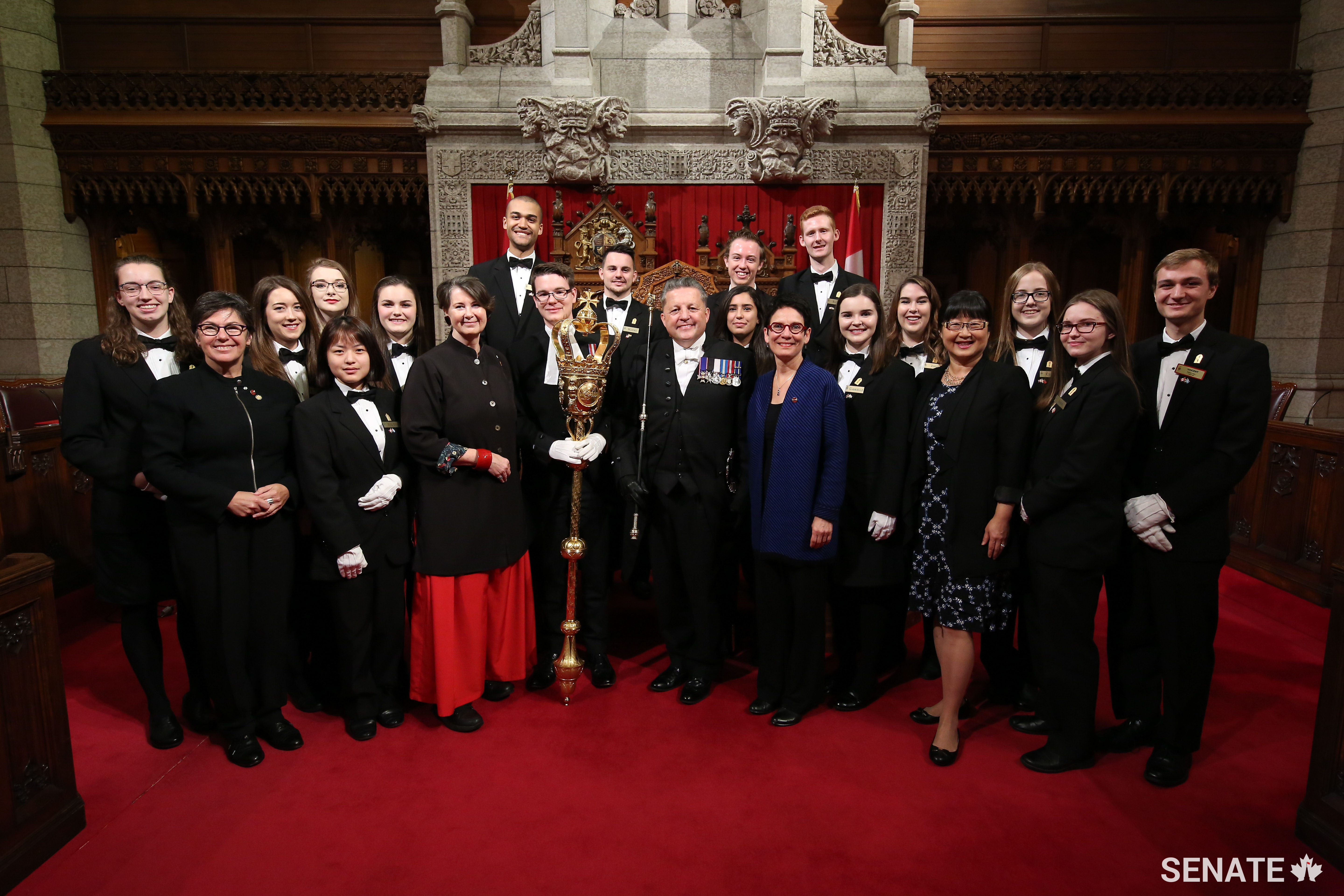 The Senate pages are joined in front of the throne by Senator Kim Pate, Senator Marilou McPhedran, Usher of the Black Rod J. Greg Peters, Senator Raymonde Gagné and Senator Yonah Martin.