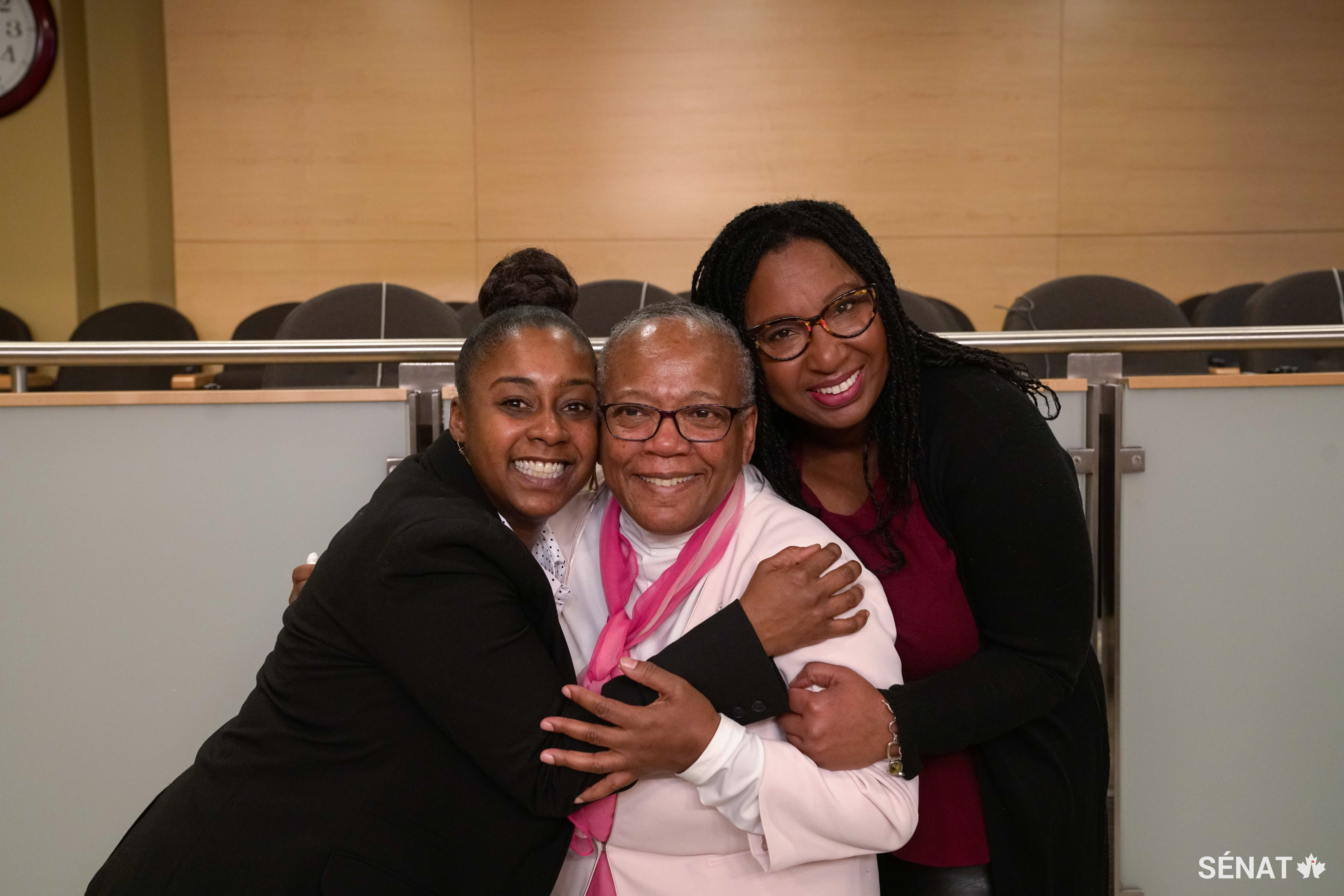 L'ancienne prisonnière fédérale Natalie Charles, à gauche, partage une accolade avec la présidente du comité, la sénatrice Wanda Thomas Bernard, au centre, et la conseillère de Mme Charles, Sophia Brown Ramsay, à droite, à la suite de son témoignage devant le comité.