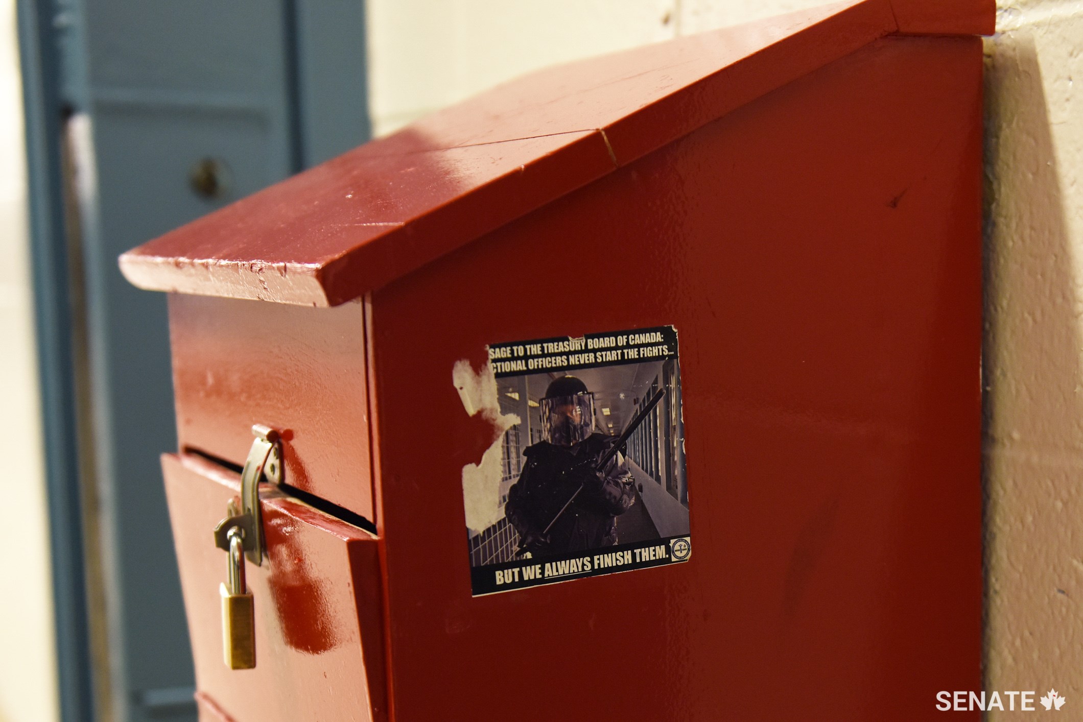 A box for prisoner complaints bears a worn sticker of a guard in full riot gear that reads in part: “Correctional officers never start the fights. But we always finish them.”