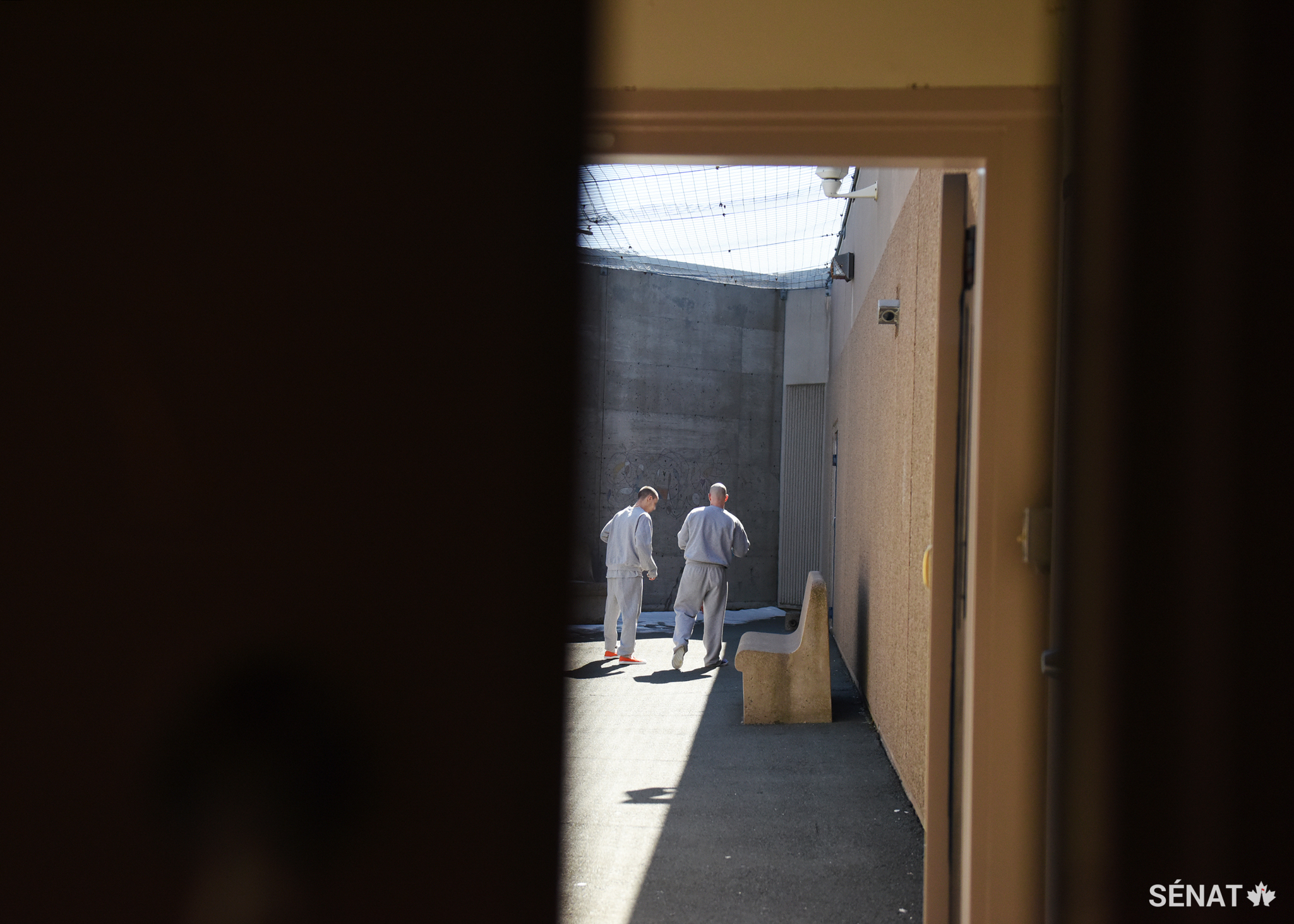 Deux résidants du East Coast Forensic Hospital font le maximum d’exercice sous les rayons du soleil qui traversent le treillis métallique mis en place pour empêcher que des marchandises de contrebande soient lancées dans la prison de l’extérieur. Comme il s’agit d’un hôpital et d’un établissement correctionnel, la sécurité est élevée — la plupart des personnes qui vivent ici ont eu des démêlés avec la loi en raison d’une maladie mentale.