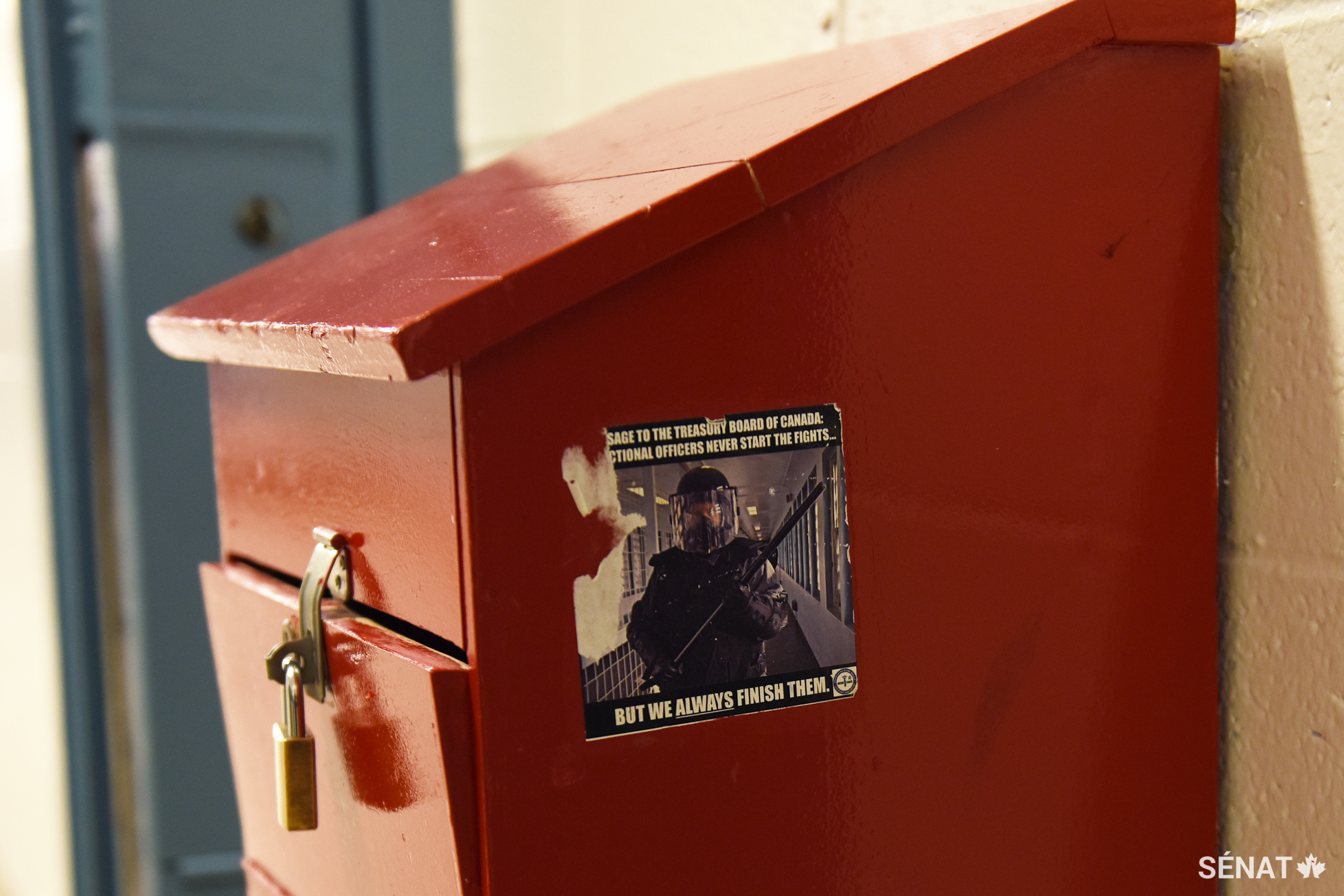Sur une boîte où les prisonniers peuvent déposer leurs plaintes, on voit un autocollant qui montre un gardien vêtu d’une tenue anti émeute. On peut y lire que les agents correctionnels ne commencent jamais les batailles, mais qu’ils y mettent toujours fin.