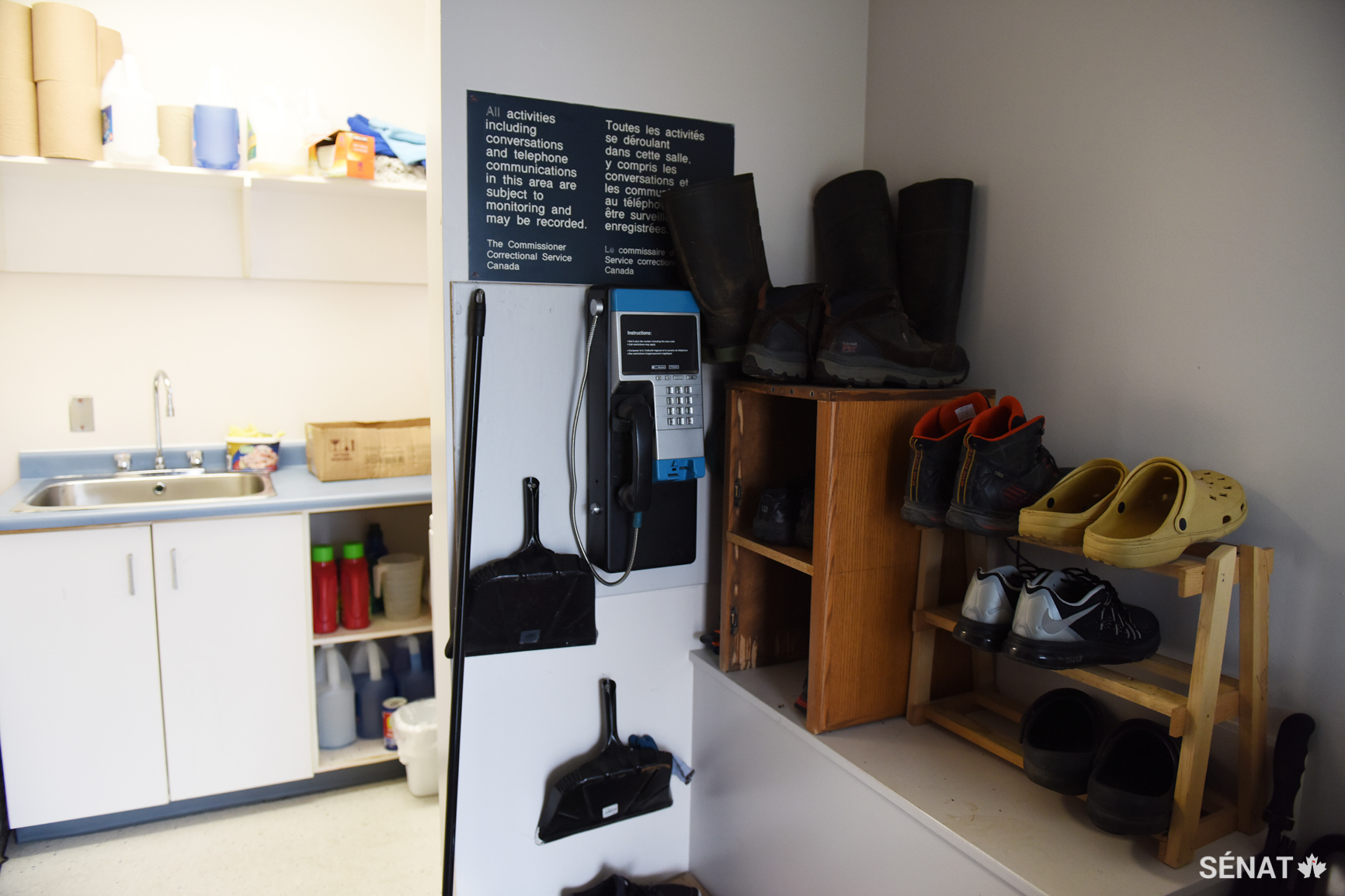 Un téléphone public et des chaussures à l’entrée d’une unité d’habitation à sécurité minimale où vivent six hommes.