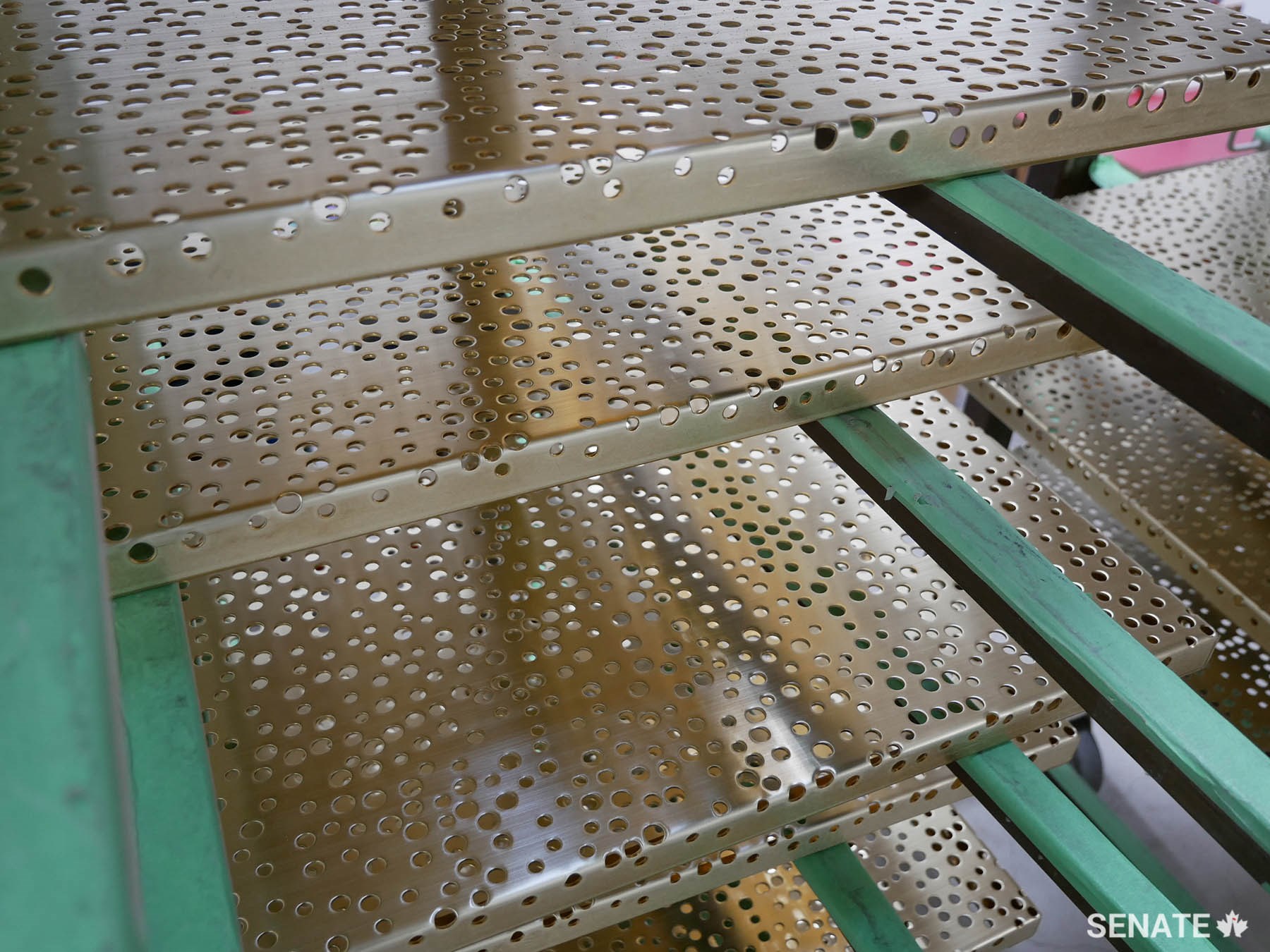 During manufacturing, perforated bronze panels sit on drying racks between chemical baths.