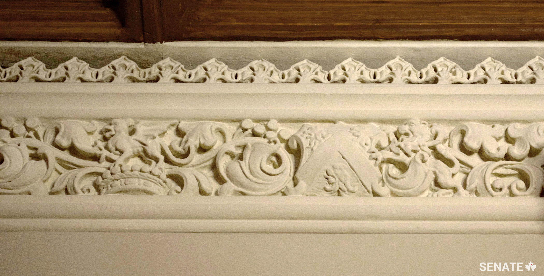 The elements of Lord Monck’s coat of arms appear in an unconventional side-by-side arrangement within the narrow cornice. They include a viscount’s coronet with a dragon crest and a shield displaying three lions’ heads.