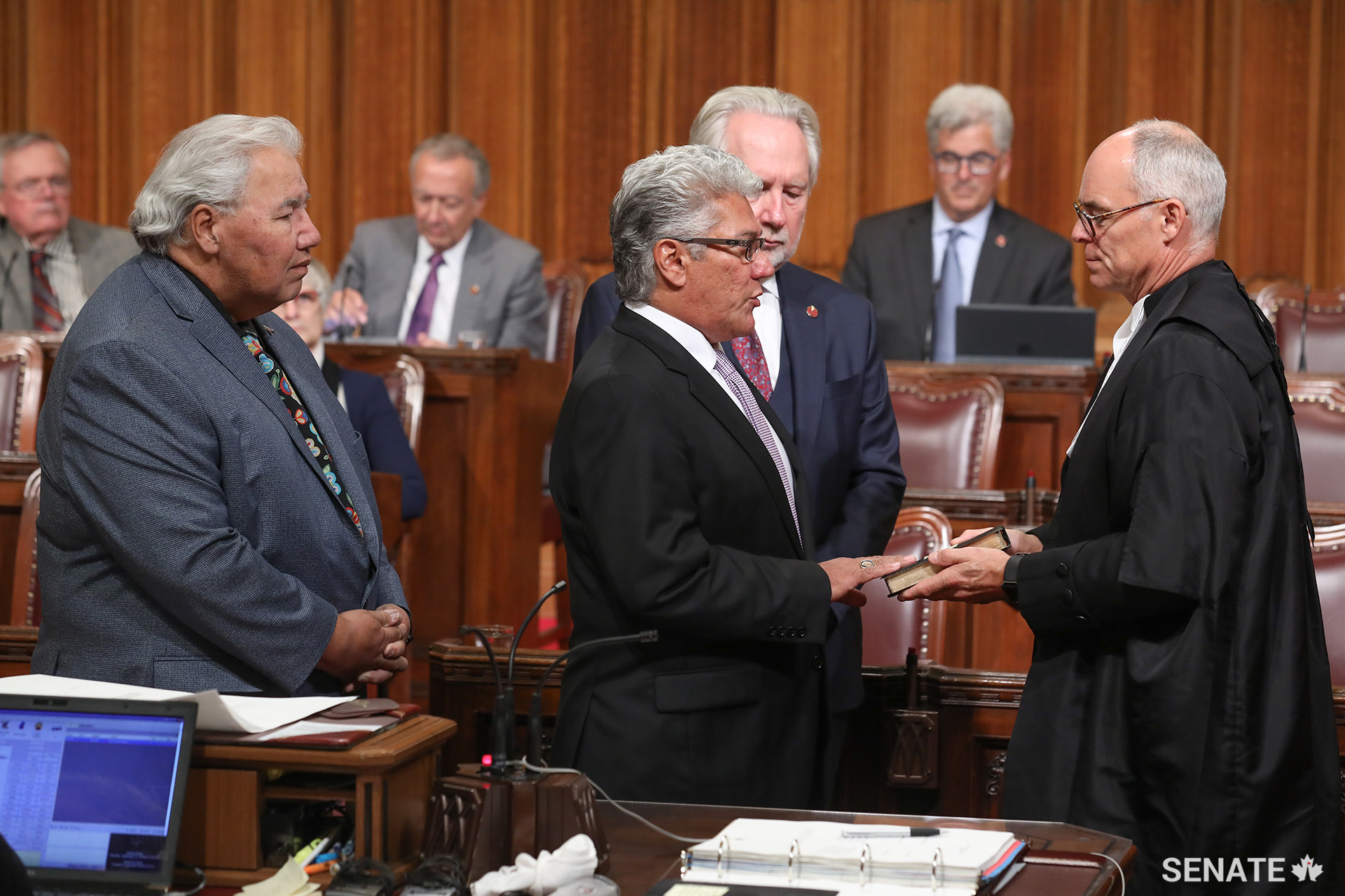 Senator Marty Klyne is sworn in during a ceremony in the Red Chamber as Senators Murray Sinclair and Peter Harder look on.