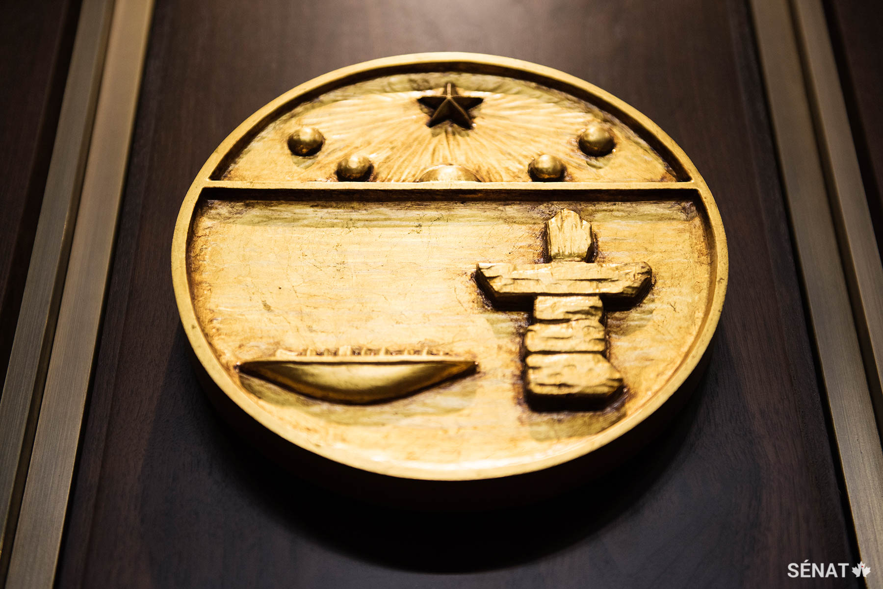 Sur l’écu du Nunavut, le soleil de minuit et l’étoile Polaire surplombent un qulliq, lampe à l’huile inuite traditionnelle, et un inuksuk, construction en pierre qui sert à guider les voyageurs.