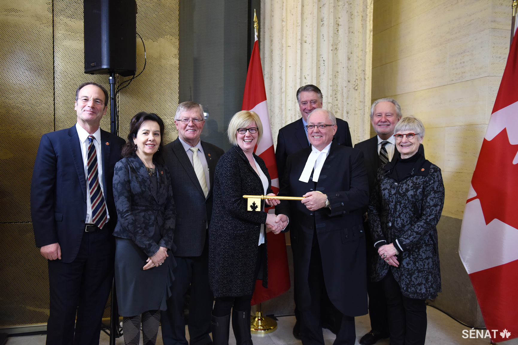La ministre des Services publics et de l’Approvisionnement et de l’Accessibilité, Carla Qualtrough, remet au Président du Sénat, George J. Furey, la clé du nouvel édifice du Sénat du Canada, soulignant ainsi la cession officielle de l’édifice qui sera la résidence temporaire du Sénat pendant la réfection de l’édifice du Centre. Les sénateurs Marc Gold, Raymonde Saint-Germain, Donald Plett, Scott Tannas, Peter Harder et Patricia Bovey se joignent à eux pour le transfert officiel.