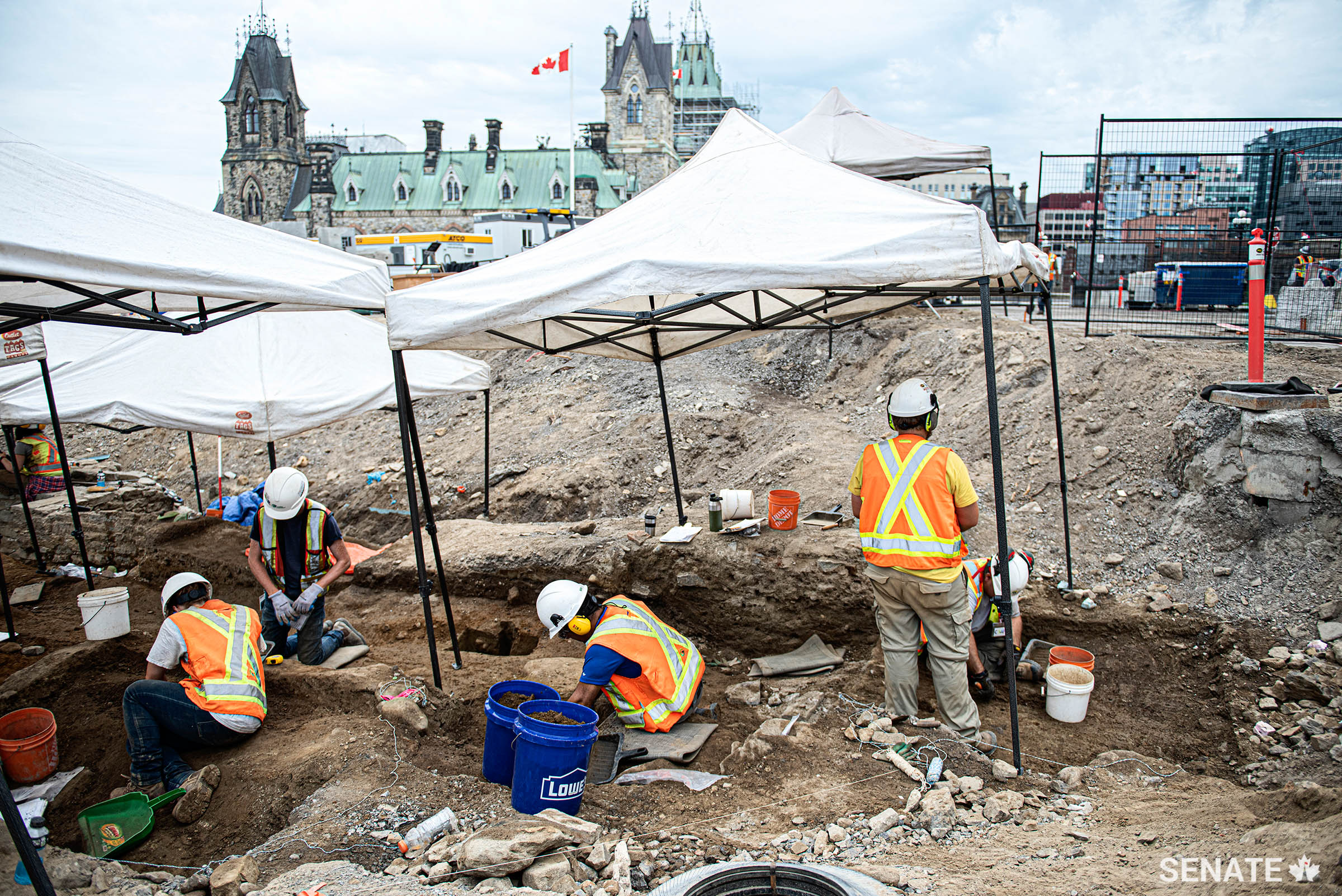 Archaeologists excavate the site of a 19th-century guardhouse on Parliament Hill, with the East Block building in the background.