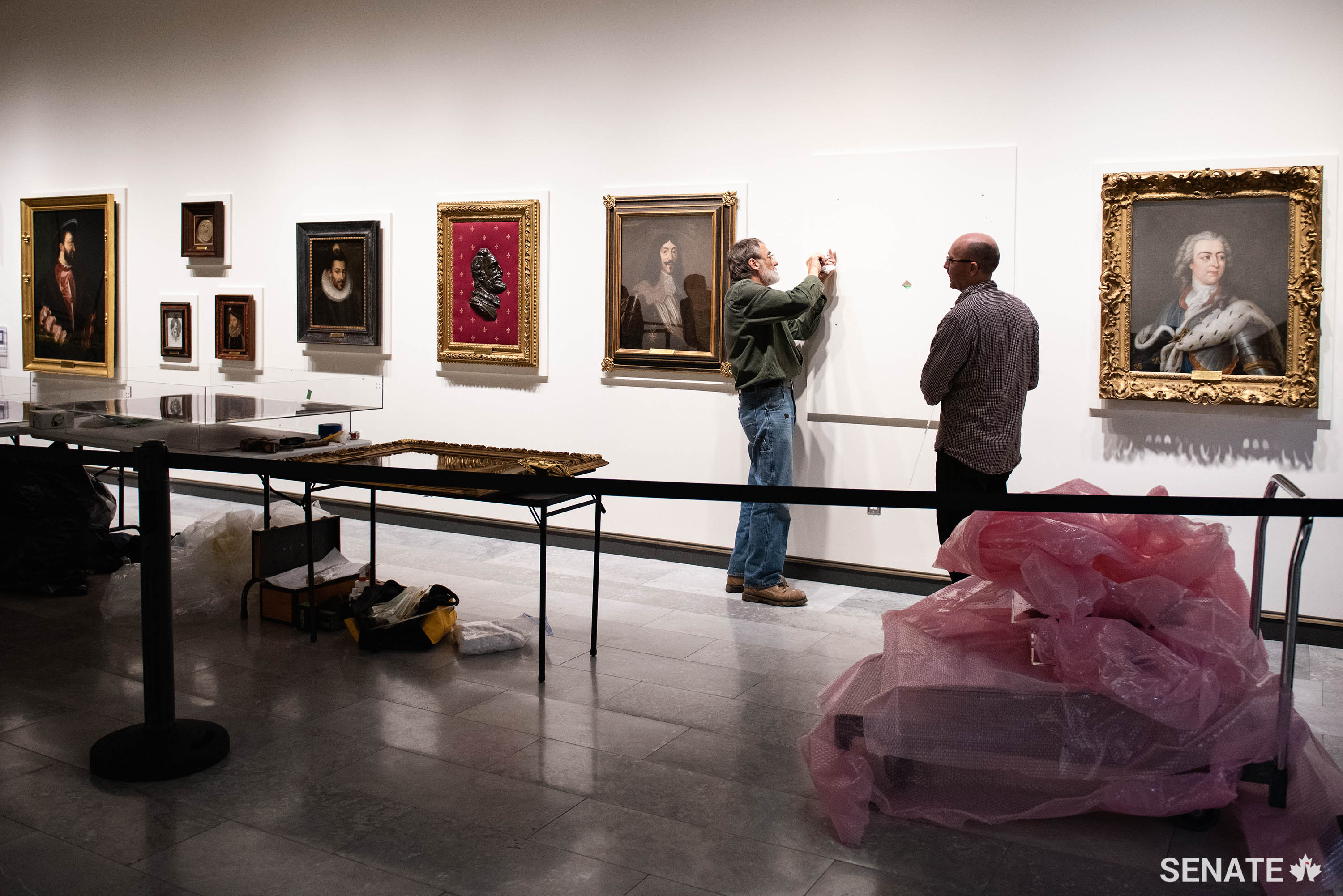 Exhibition preparators make adjustments to the mounting for the portrait of the Sun King, Louis XIV. During his 72-year-long reign, France became Europe’s leading power and France’s colonies prospered after he signed a peace accord with the Haudenosaunee (Iroquois) Confederacy in 1701. To his right is a portrait of his great-grandson and heir, King Louis XV, who couldn’t live up to his famous great-grandfather. Louis XV’s forces were driven out of New France during the Seven Years War and the power of the French monarchy began its decline.