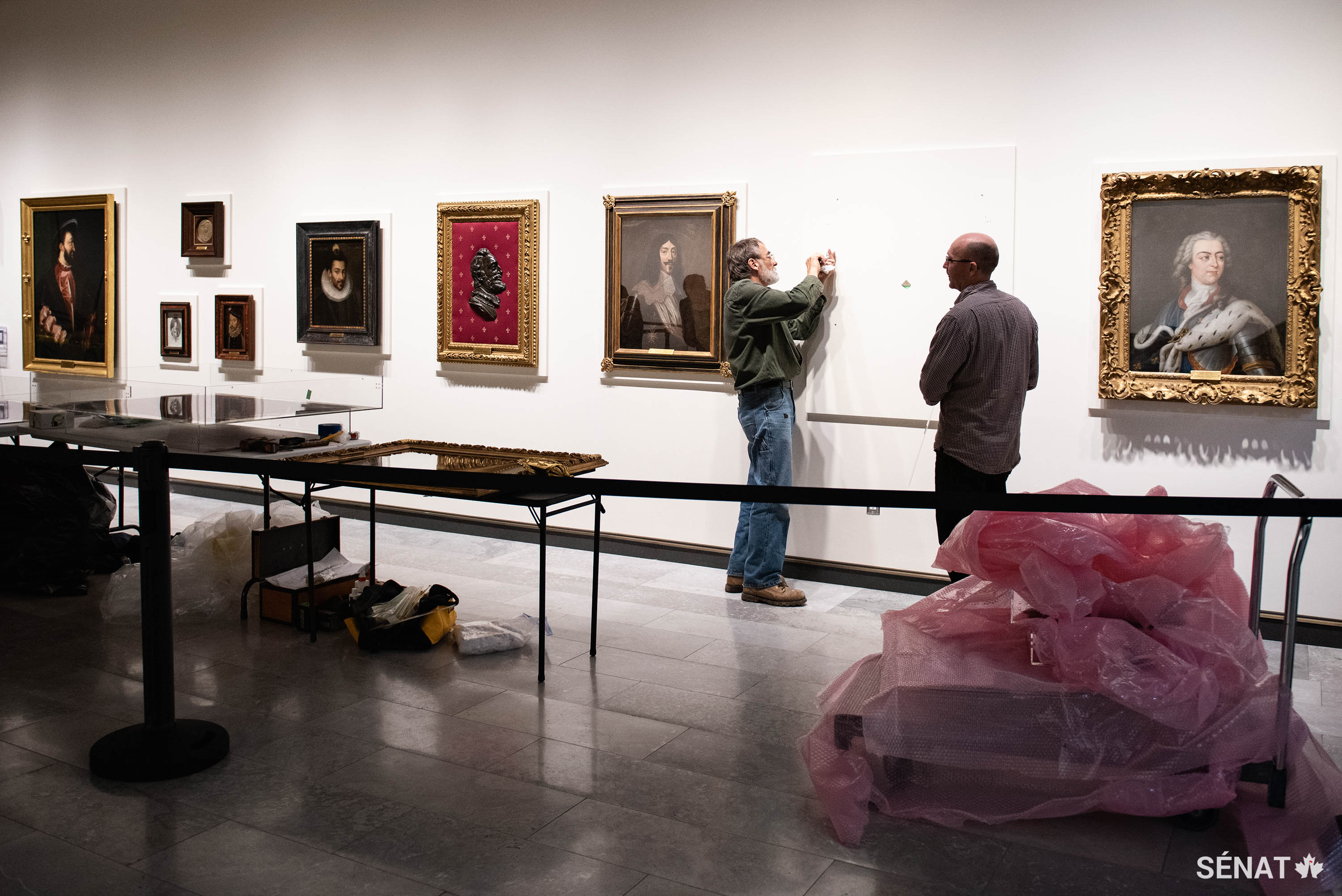 Les préparateurs d’exhibition ajustent le montage du portrait du Roi Soleil, Louis XIV. Pendant son règne, qui a duré 72 ans, la France est devenue la principale puissance européenne, et ses colonies ont prospéré après la signature d’un accord de paix avec la Confédération Haudenosaunee (peuple iroquois) en 1701. À la droite de Louis XIV se trouve le portrait de son arrière-petit-fils et héritier, le roi Louis XV, qui n’est pas parvenu à suivre les traces de son illustre arrière-grand-père. Les forces de Louis XV ont été repoussées à l’extérieur de la Nouvelle France après la guerre de Sept Ans et le pouvoir de la monarchie française a commencé à décliner.