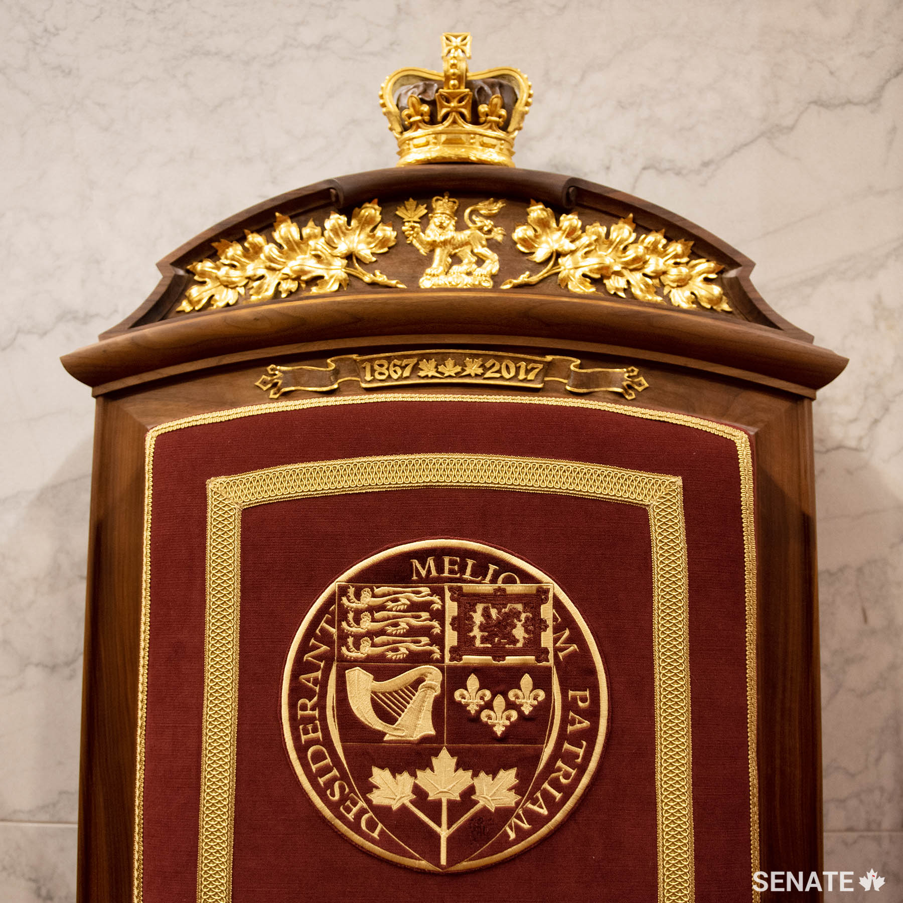 The lion crest from the Arms of Canada appears in the headpiece of the consort’s throne. The shield from the Arms of Canada is embroidered on the upholstery. The dates 1867-2017, carved into the chairback, commemorate Canada’s sesquicentennial.