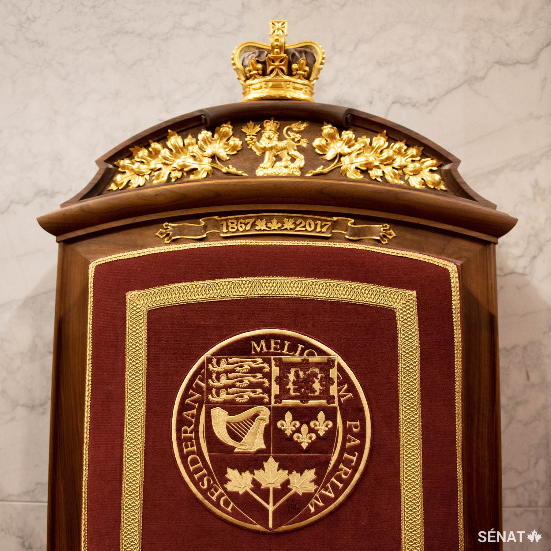 Le lion, qui fait partie des armoiries du Canada, figure sur la tête du trône du consort. L’écu des armoiries du Canada est brodé dans le tissu du fauteuil. Les dates 1867-2017, gravées sur le dossier du fauteuil, soulignent le 150e anniversaire du Canada.