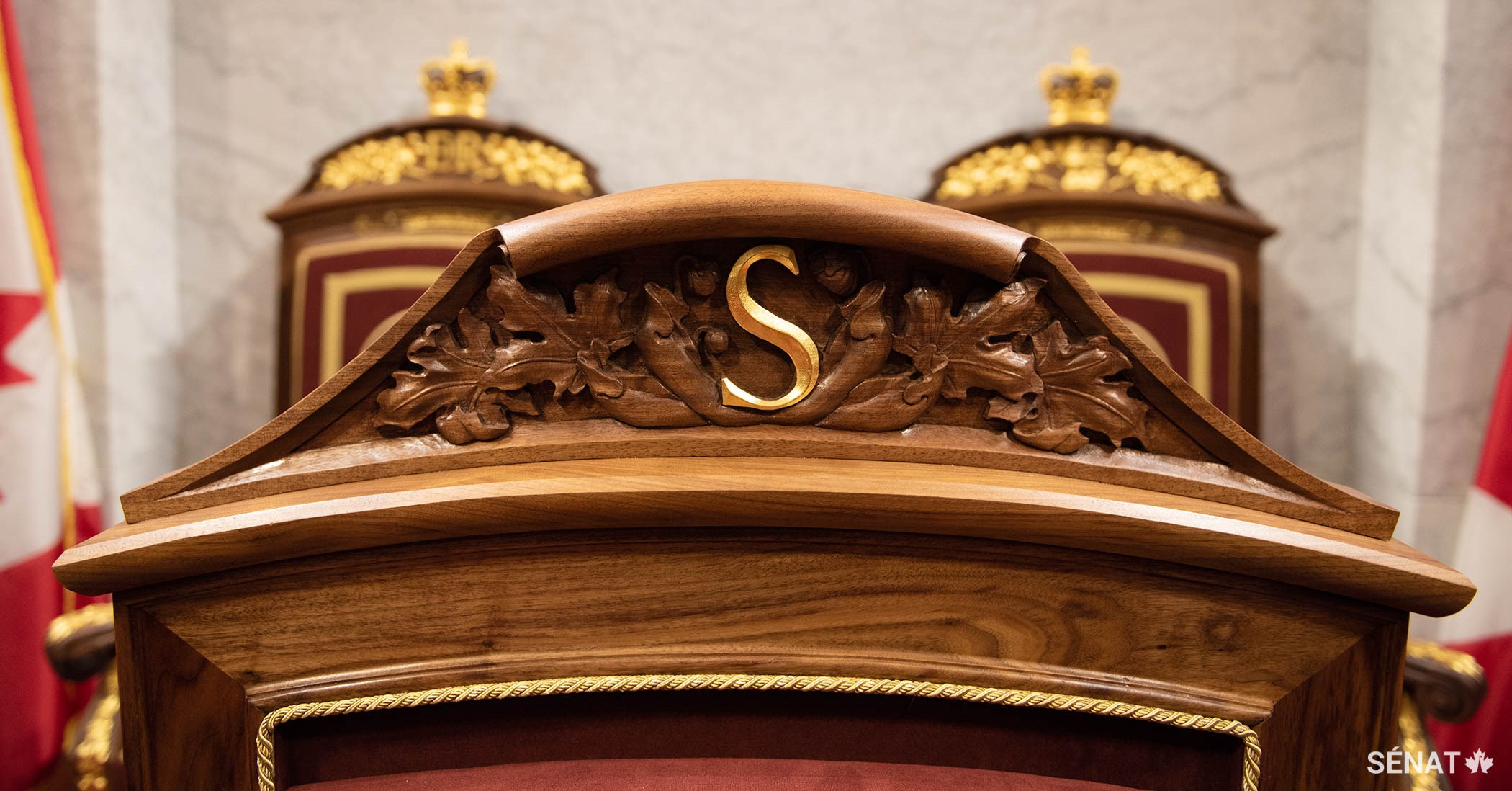 La lettre S, qui représente le mot « Sénat », est gravée dans la tête du fauteuil du Président du Sénat. Elle est entourée de feuilles d’érable.