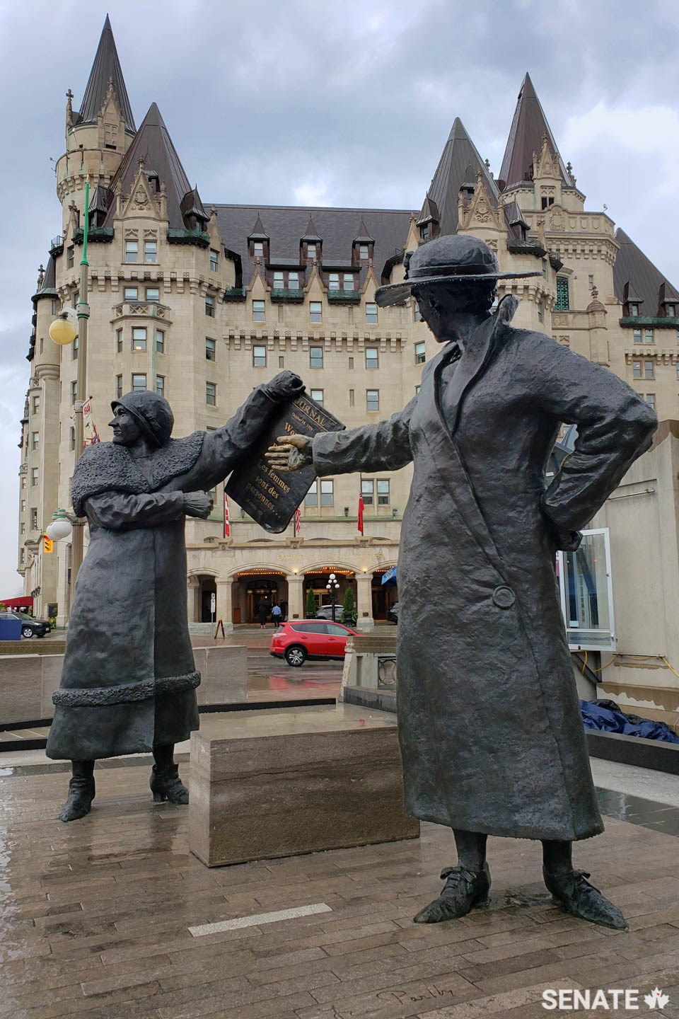 Irene Parlby gestures toward Nellie McClung who holds a newspaper announcing their victory in the Persons Case.
