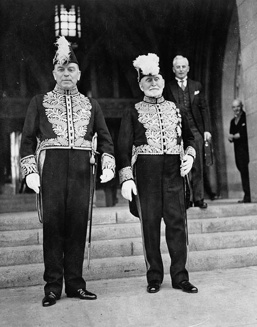Prime Minister William Lyon Mackenzie King, left, and Senator Dandurand appear in state uniform in front of Centre Block’s Peace Tower in 1939. (Photo credit: <a href='https://www.bac-lac.gc.ca/eng/CollectionSearch/Pages/record.aspx?app=FonAndCol&IdNumber=3194612' target='_blank'>Library and Archives Canada</a>)