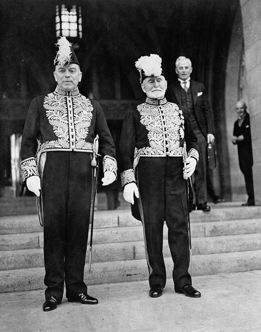 Prime Minister Le premier ministre William Lyon Mackenzie King, à gauche, et le sénateur Dandurand portent la tenue officielle devant la Tour de la Paix de l’édifice du Centre en 1939. (Crédit photo : <a href='https://www.bac-lac.gc.ca/eng/CollectionSearch/Pages/record.aspx?app=FonAndCol&IdNumber=3194612' target='_blank'>Bibliothèque et Archives Canada</a>)
