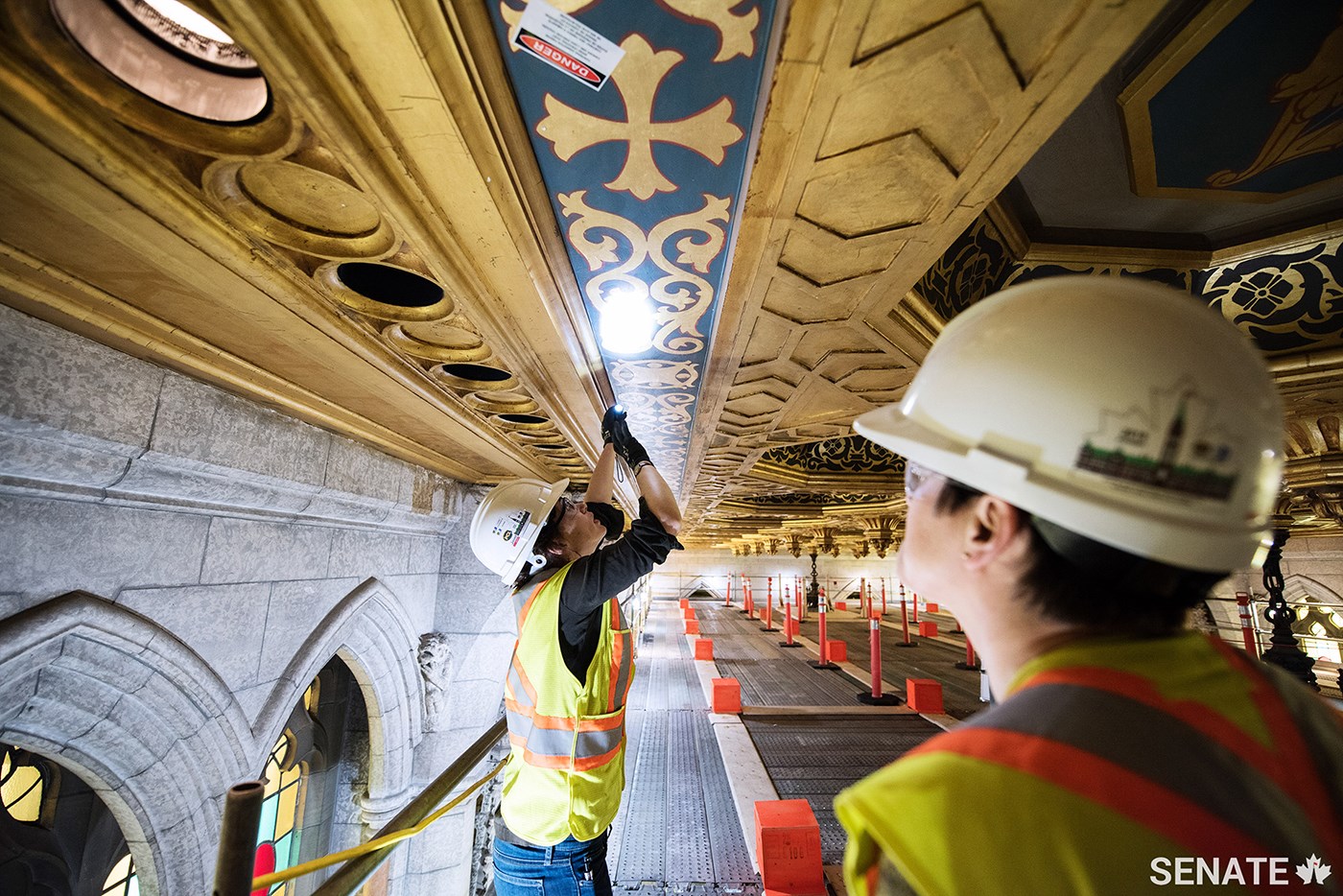 Hirst Conservation’s Caroline Wright, who specializes in architectural paint research, examines a detail from the Senate ceiling as Kate Westbury, Public Services and Procurement Canada’s heritage lead for the Centre Block Rehabilitation Program, looks on.