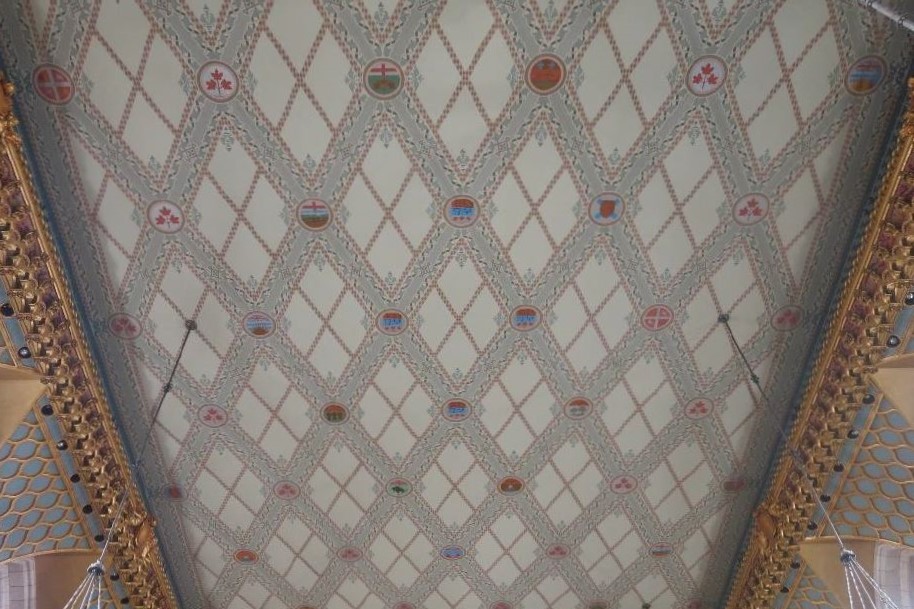 Orné de symboles provinciaux, le treillis du plafond de la Chambre des communes cache les coutures des panneaux de lin. (Crédit photo : Legris Conservation)