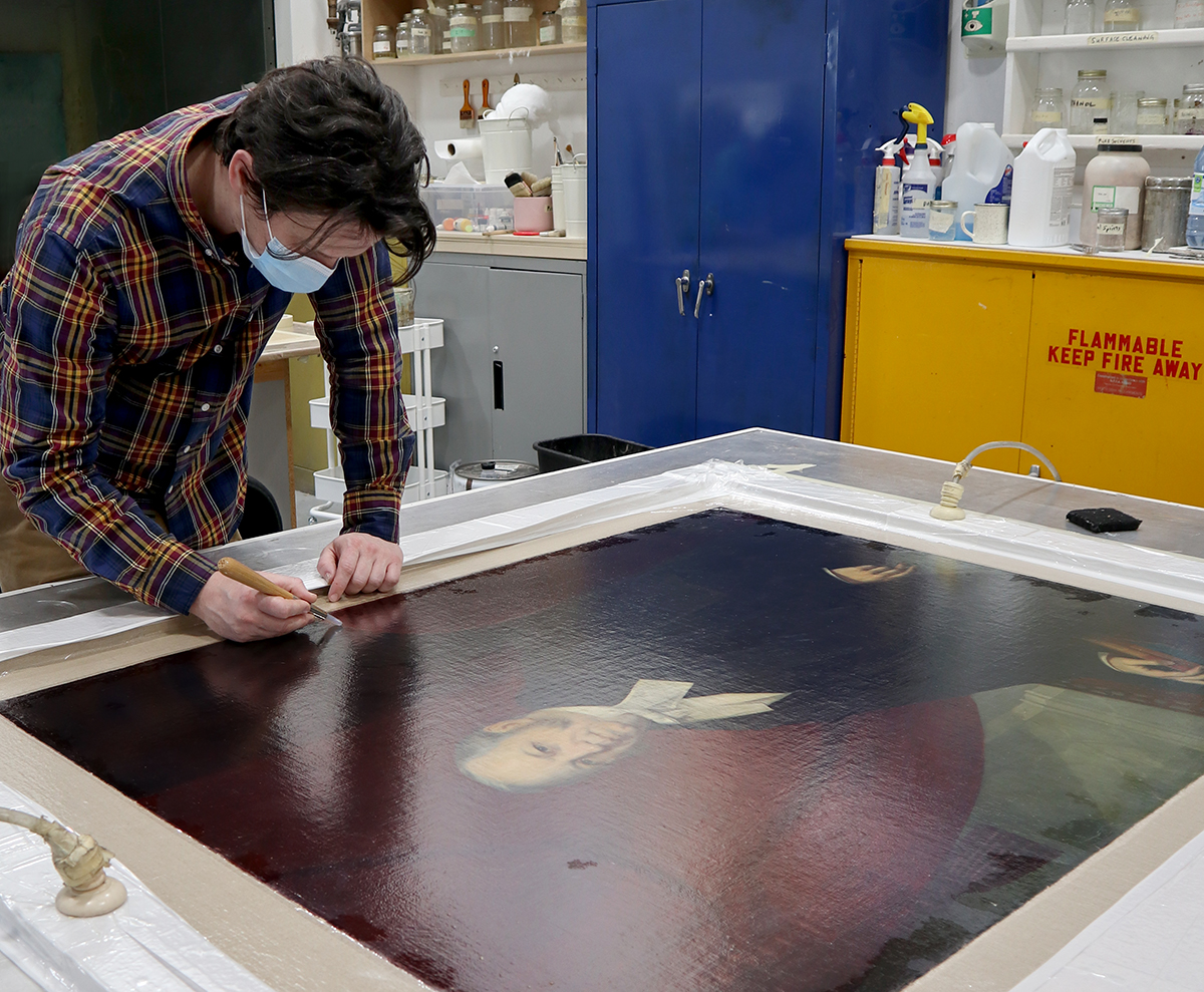 Conservator John Legris uses a soft-tipped burnishing tool to help set down areas of cracking during the lining process. (Photo credit: Legris Conservation)