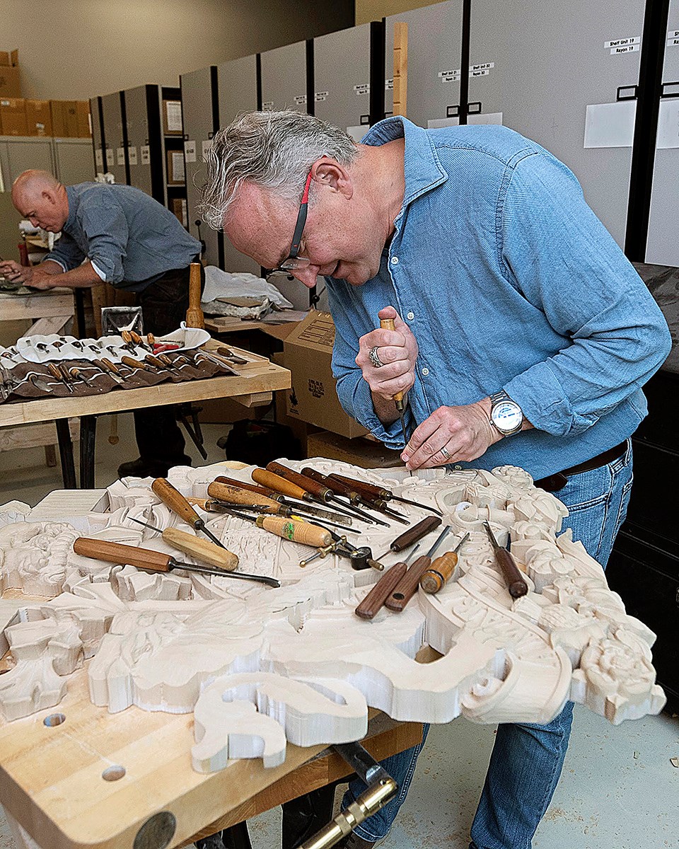 Mr. White carves a depiction of the Arms of Canada in high-density polyurethane foam board, a modern alternative to wood, in 2017. The piece, which now hangs in the temporary Senate Chamber in the Senate of Canada Building, was finished in a tissue-thin veneer of metallic leaf that makes the carving look like it was cast in metal. (Photo credit: Public Services and Procurement Canada)