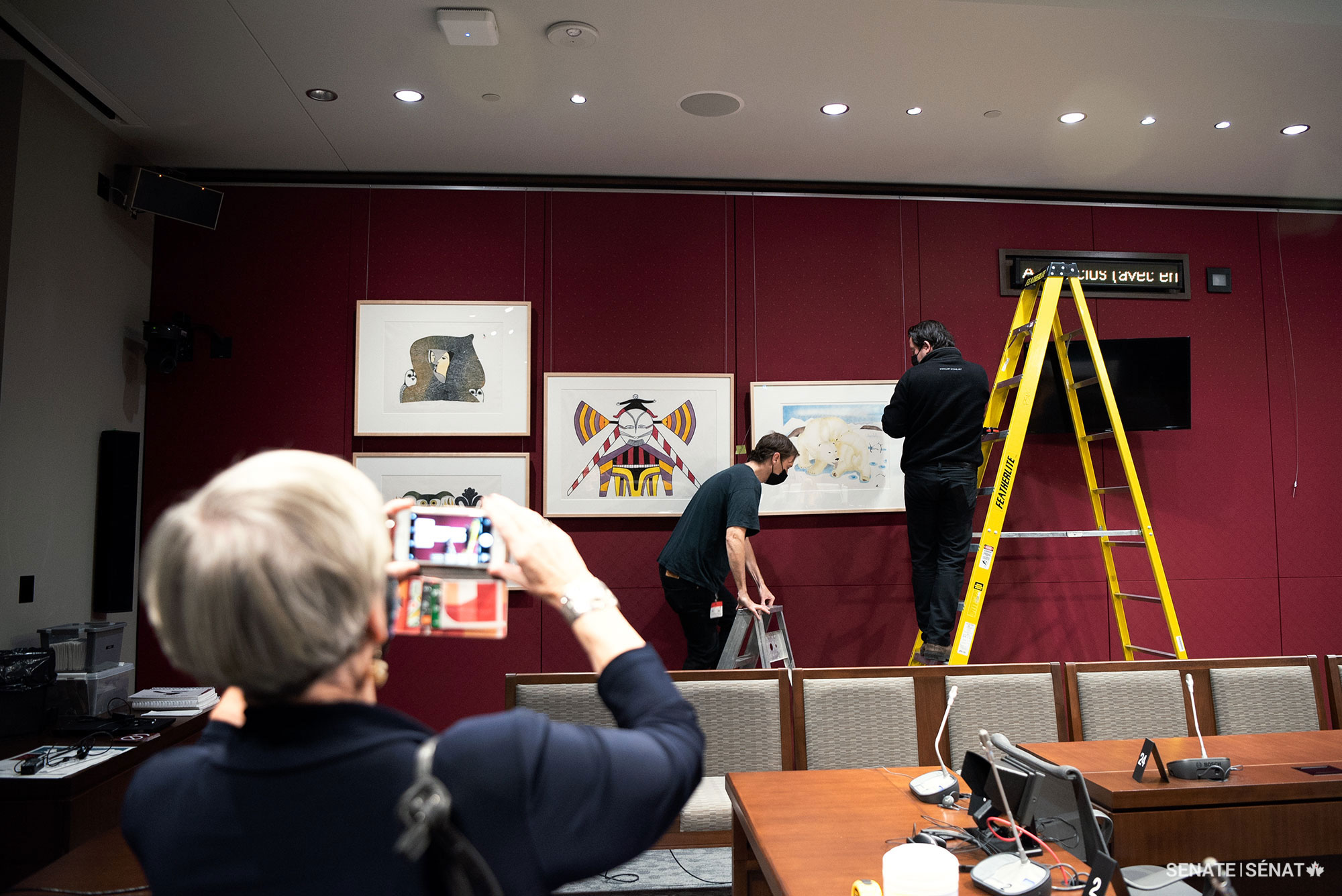Senator Bovey watches as works from the Winnipeg Art Gallery-Qaumajuq are installed in the Senate of Canada Building’s committee room B-30.