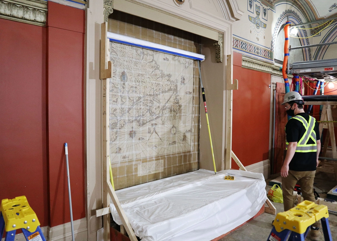 A crew preps the mural of a map in the Senate Railway Committee Room for removal. The scaffold system to remove the murals that were glued to the top of the walls can be seen to the right. (Photo credit: Legris Conservation Inc.)