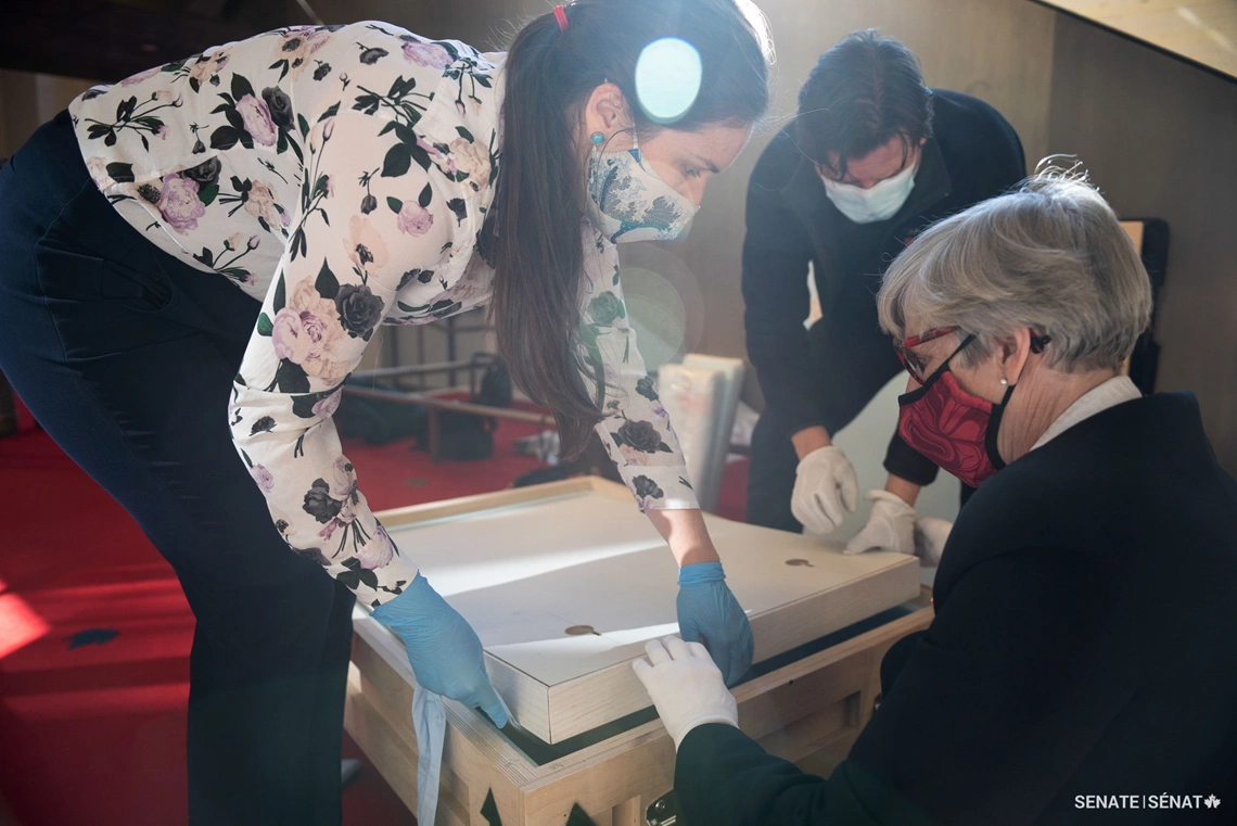 Senate Curator Tamara Dolan, left, and Senator Bovey, right, inspect the crate containing Light Laureate prior to the installation of this mixed-media piece in the Senate foyer.