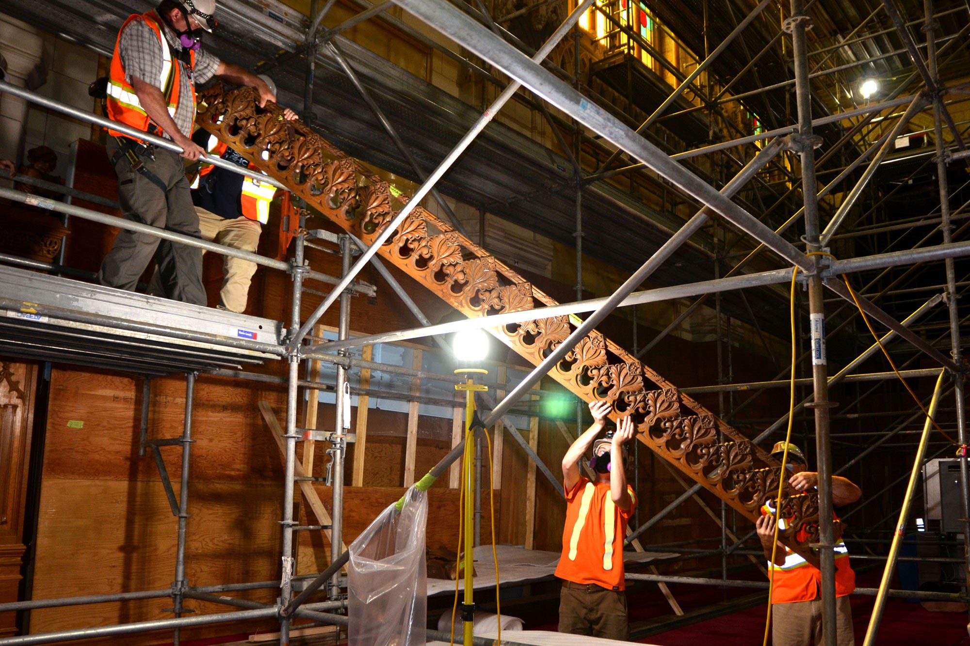 Workers carefully lower a long section of detached wooden fretwork.