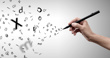 A hand holding a black pen writes in the air as scattered letters swirl and float outward against a light grey background