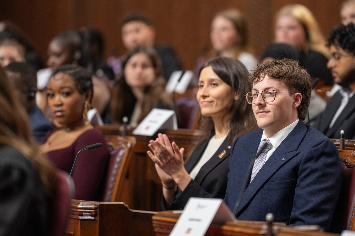 Young adults sitting at senators’ desks in the Senate Chamber.