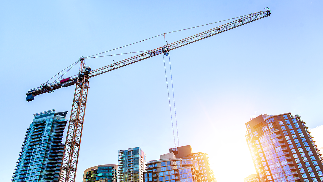 A construction crane towering over high-rise buildings at sunrise.