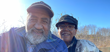 A Black man and a Black woman, both smiling and wearing hats, pictured on a sunny day.