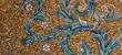 Colorful mosaic artwork with floral and vine patterns in shades of gold, green, blue, and white.