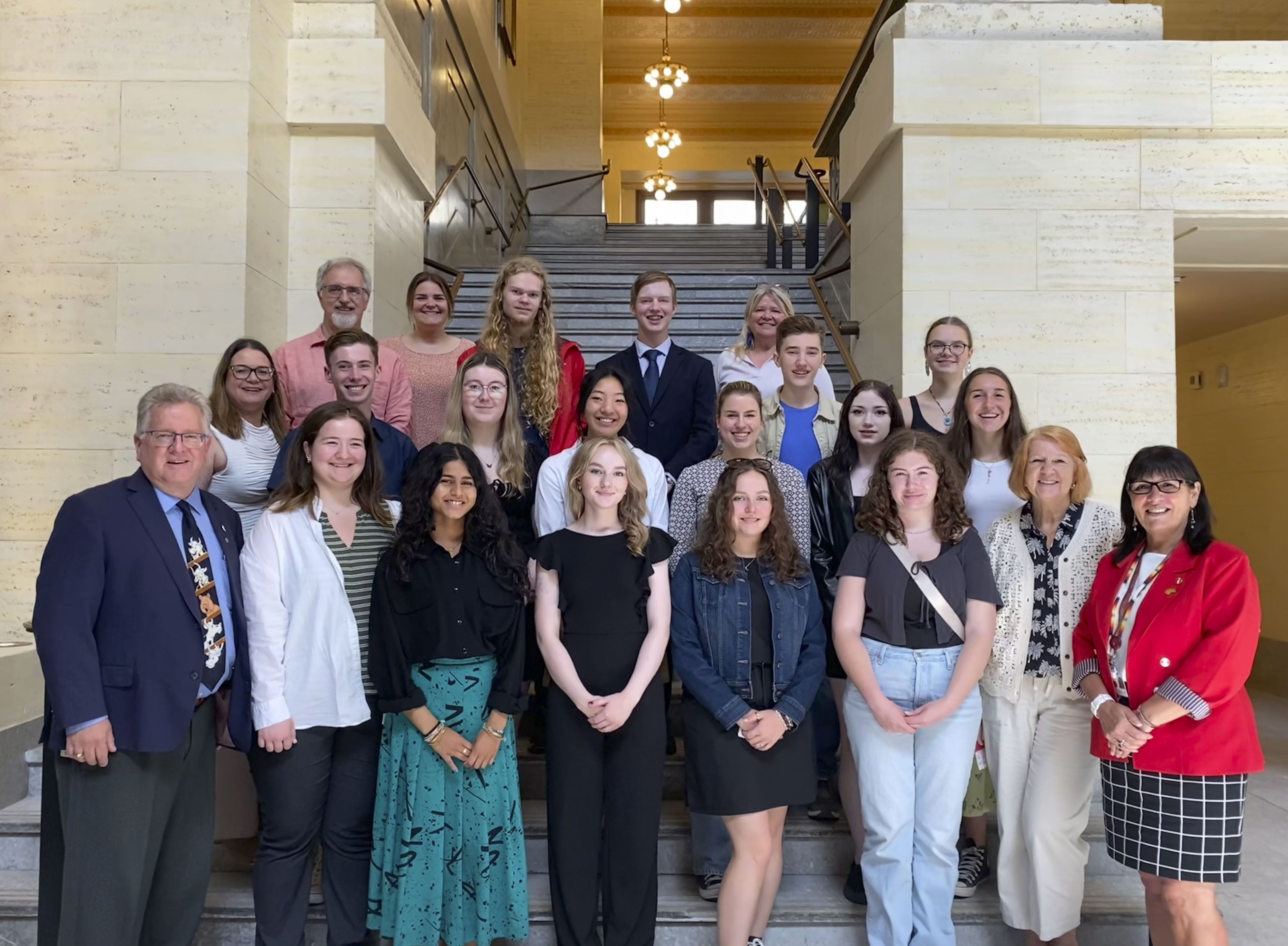 Senators Rob Black and Judy A. White stand with a group of students in the staircase of the foyer in the Senate of Canada Building.