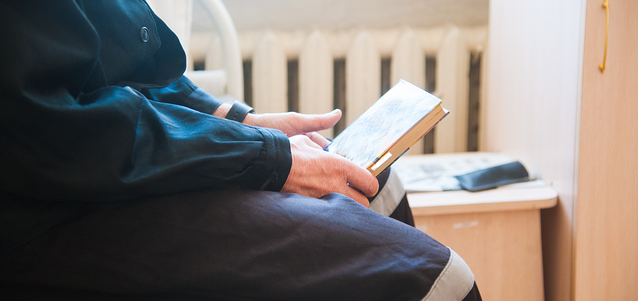 A person sitting down and holding a book in a prison cell.