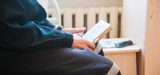 A person sitting down and holding a book in a prison cell.
