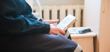 A person sitting down and holding a book in a prison cell.
