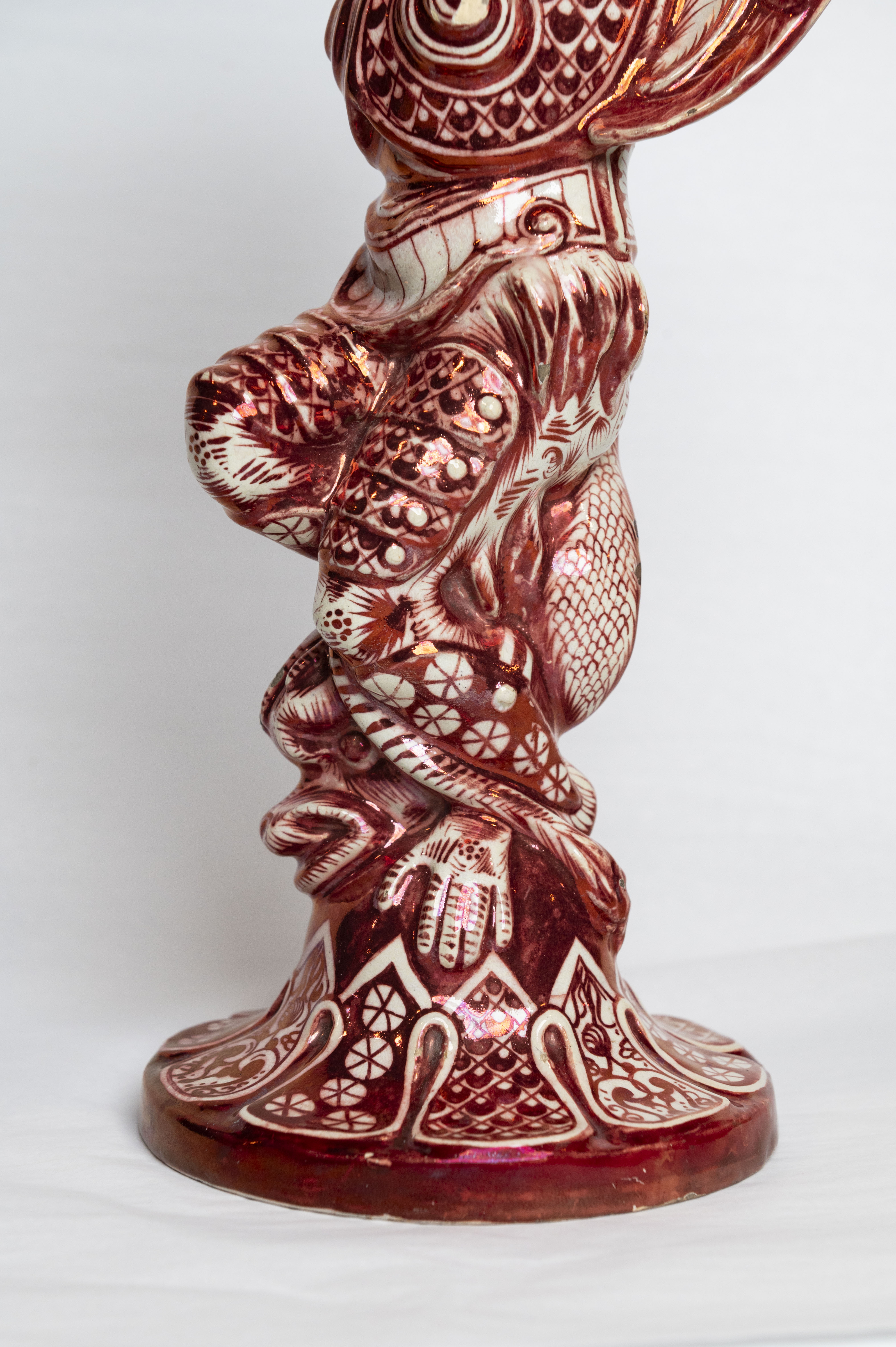 Le piédestal d’un bougeoir en céramique émaillée, représentant une grotesque avec un dauphin coincé sous ses jambes et ses pieds.