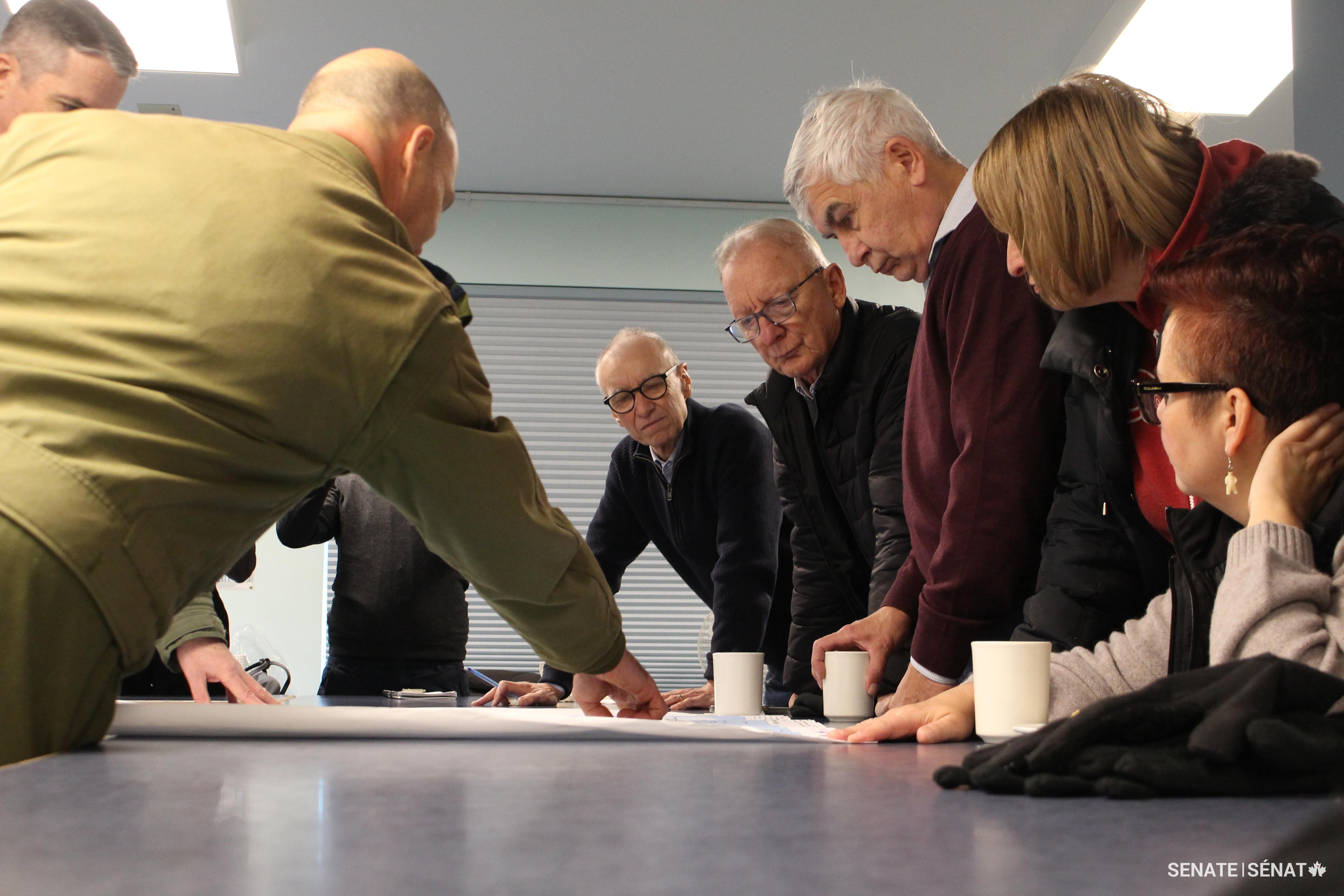 From right, senators Anderson, Dasko, Gignac, Boisvenu and Dean pore over a map of the Arctic with Canadian Armed Forces members at an Inuvik mess hall in the Northwest Territories.