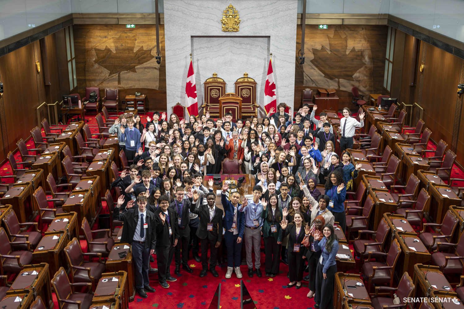 Un grand groupe de personnes se fait prendre en photo autour d’une table dans la Chambre du Sénat.